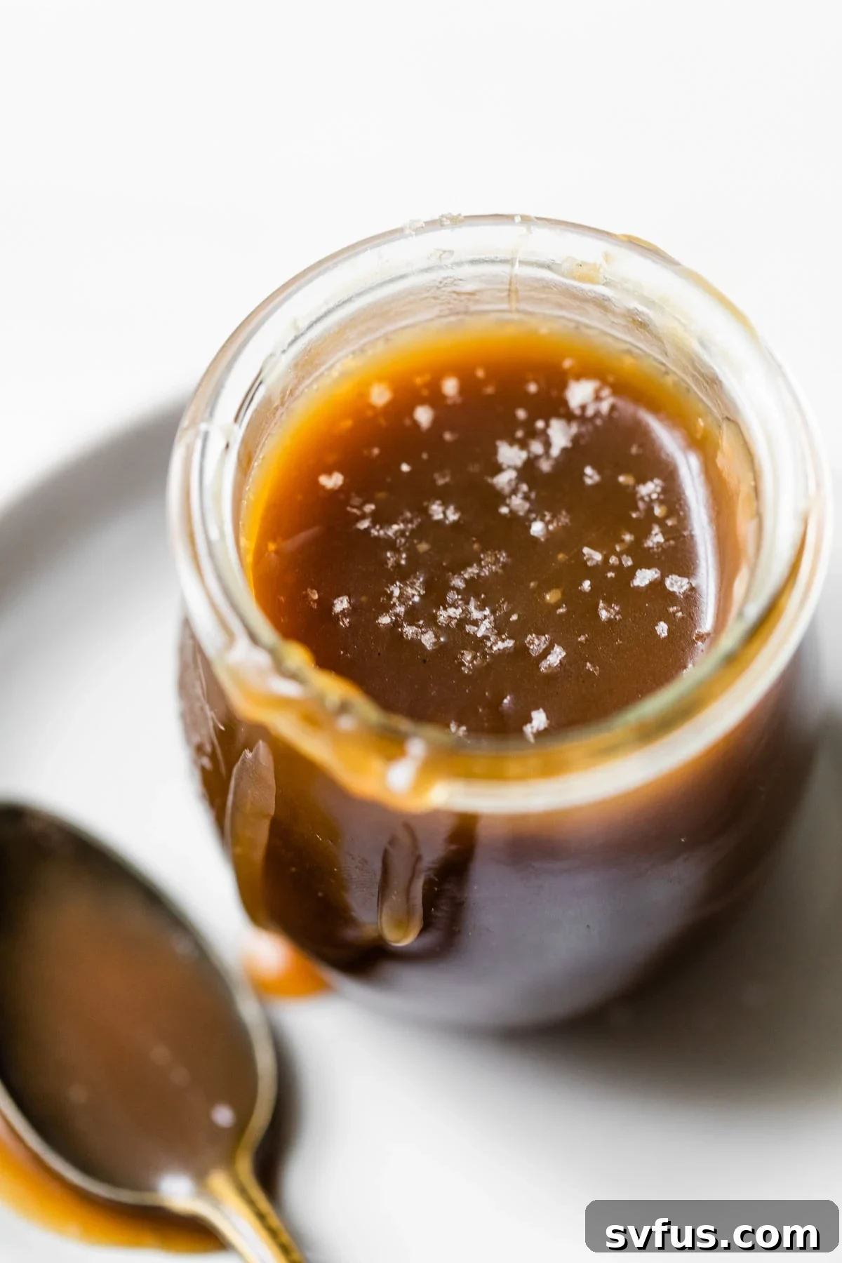 A beautifully styled glass jar brimming with thick, golden healthier salted caramel sauce, positioned on a rustic wooden surface, highlighting its rich texture and inviting appeal.