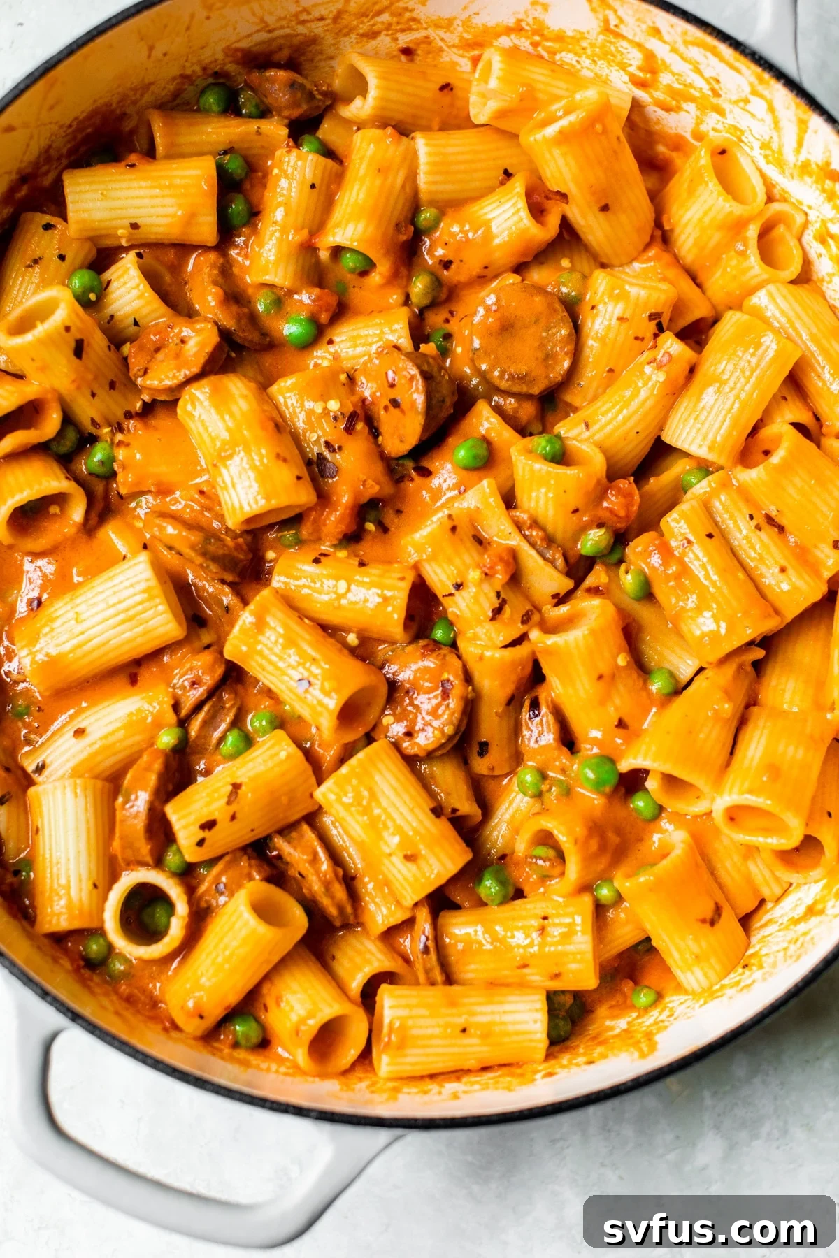 A vibrant skillet filled with Italian chicken sausage pasta, featuring golden-brown sausage, green peas, and pasta coated in a creamy red sauce.