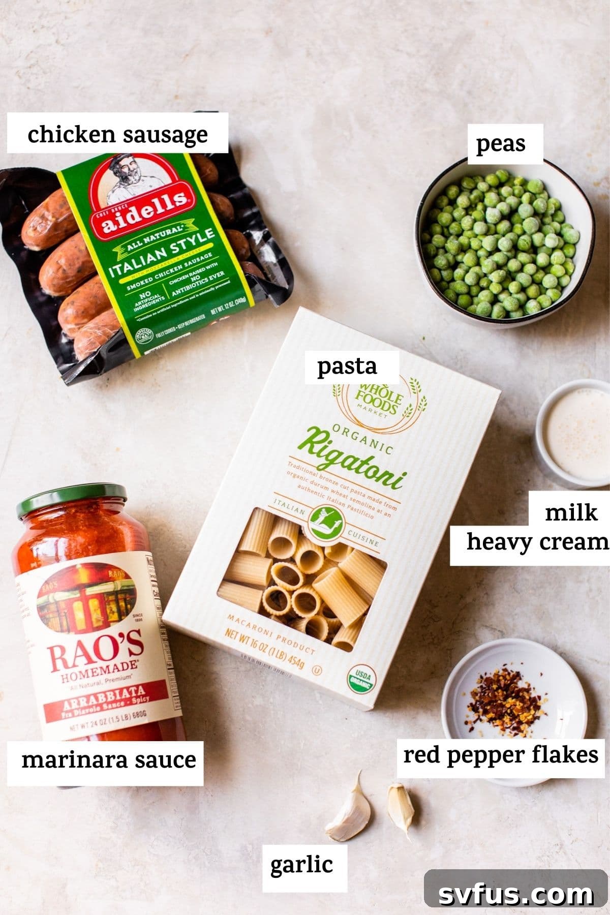 Fresh ingredients for Italian chicken sausage pasta laid out on a rustic wooden table, including uncooked pasta, chicken sausage links, marinara sauce, heavy cream, peas, garlic, and red pepper flakes.