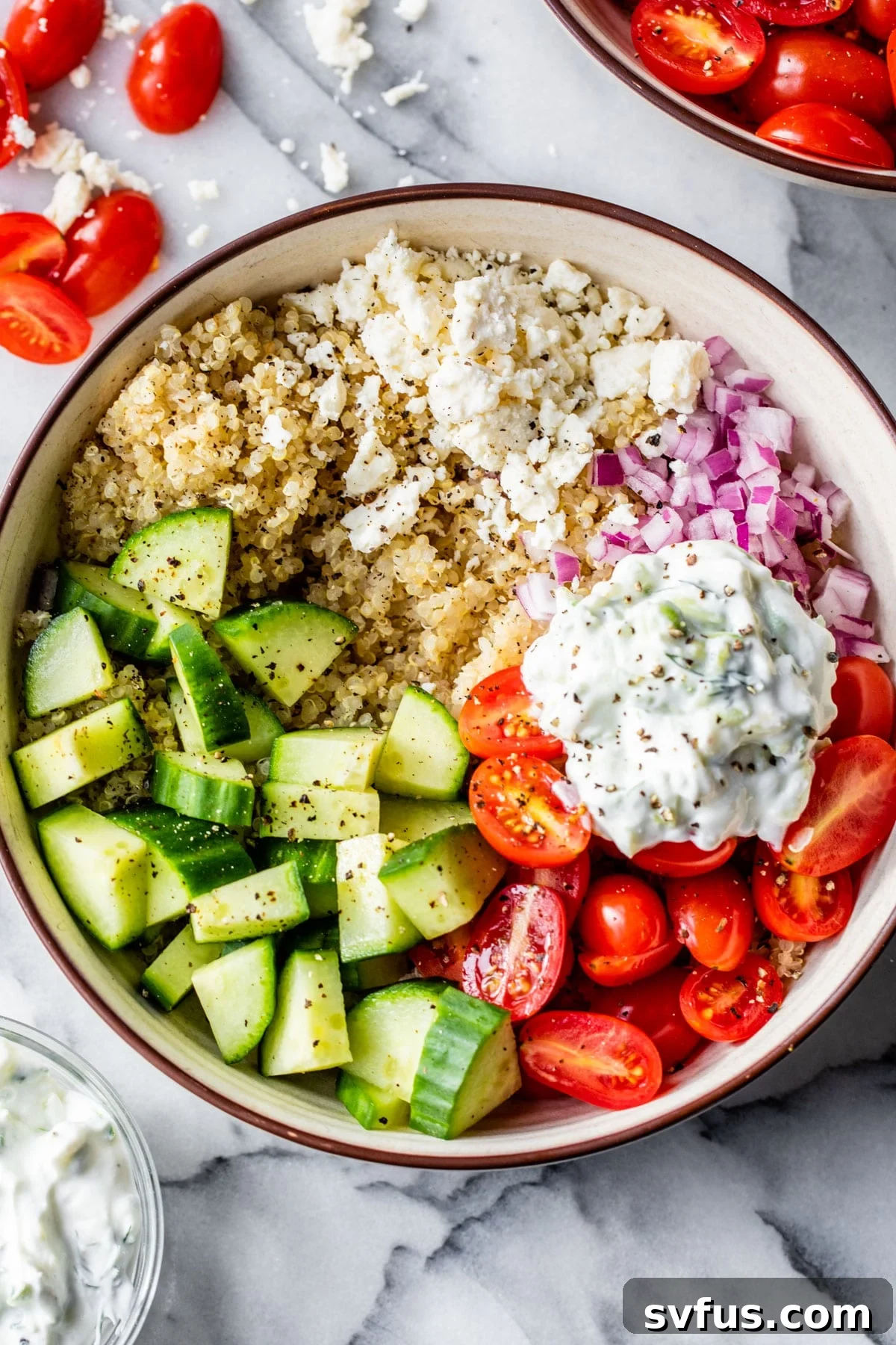 A close-up view of a Mediterranean Quinoa Bowl, showcasing vibrant tomatoes, cucumber, red onion, and crumbled feta cheese.
