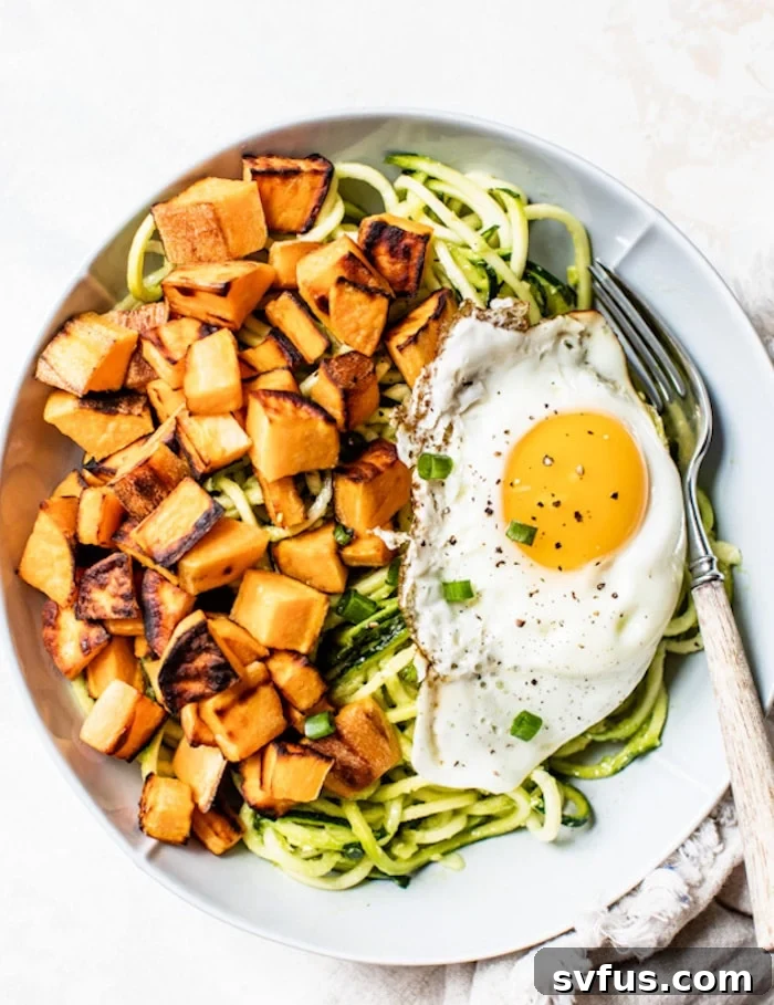 A vibrant Whole30 Zucchini Noodle Breakfast Bowl with green zucchini noodles, orange sweet potatoes, and a sunny-side-up fried egg.