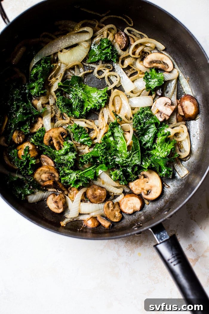 A vibrant skillet filled with perfectly caramelized onions, sautéed mushrooms, and wilted kale, forming the delicious base for the spaghetti squash.