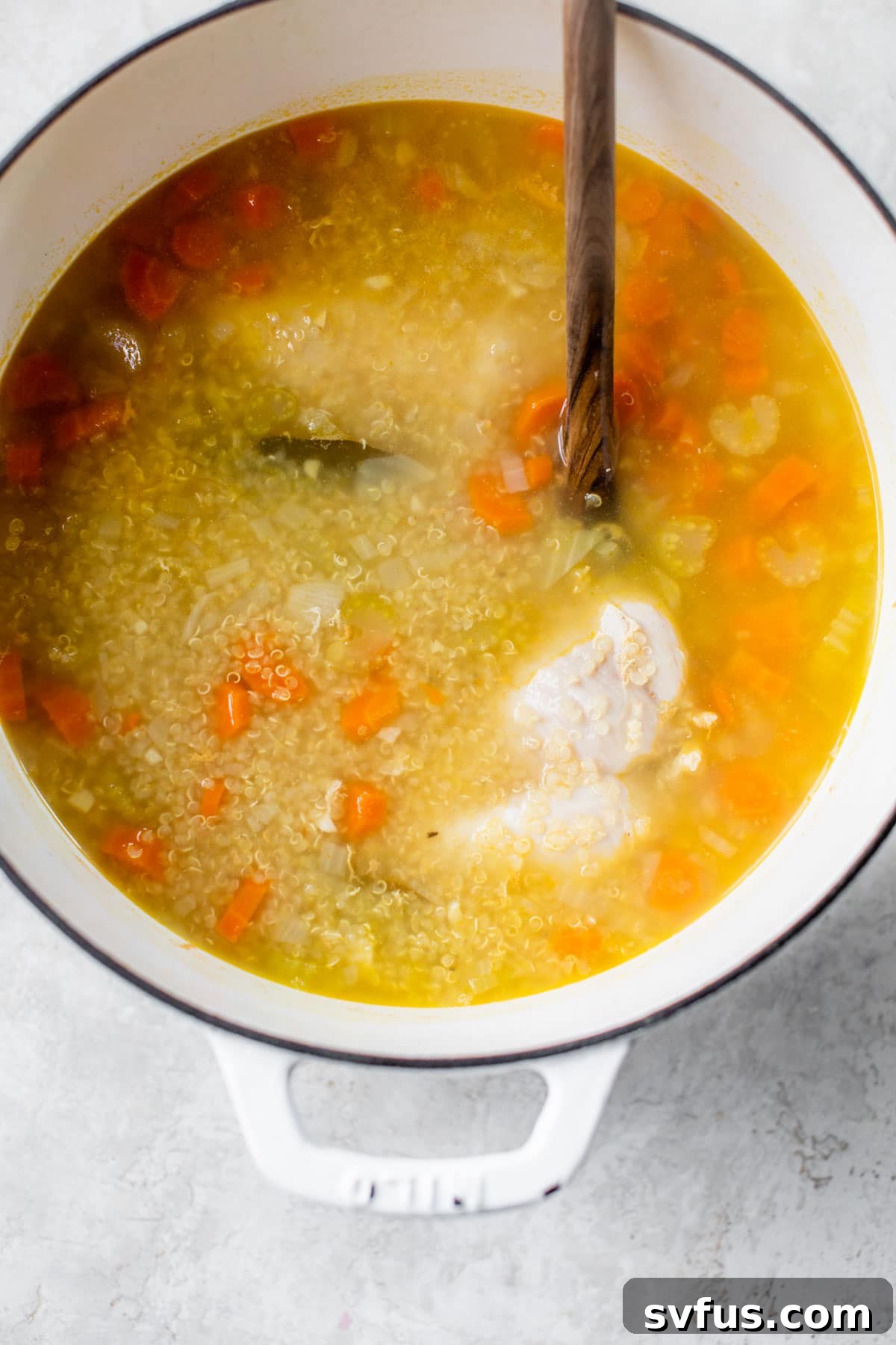 Chicken breast, quinoa, and vegetables simmering in broth in a Dutch oven.