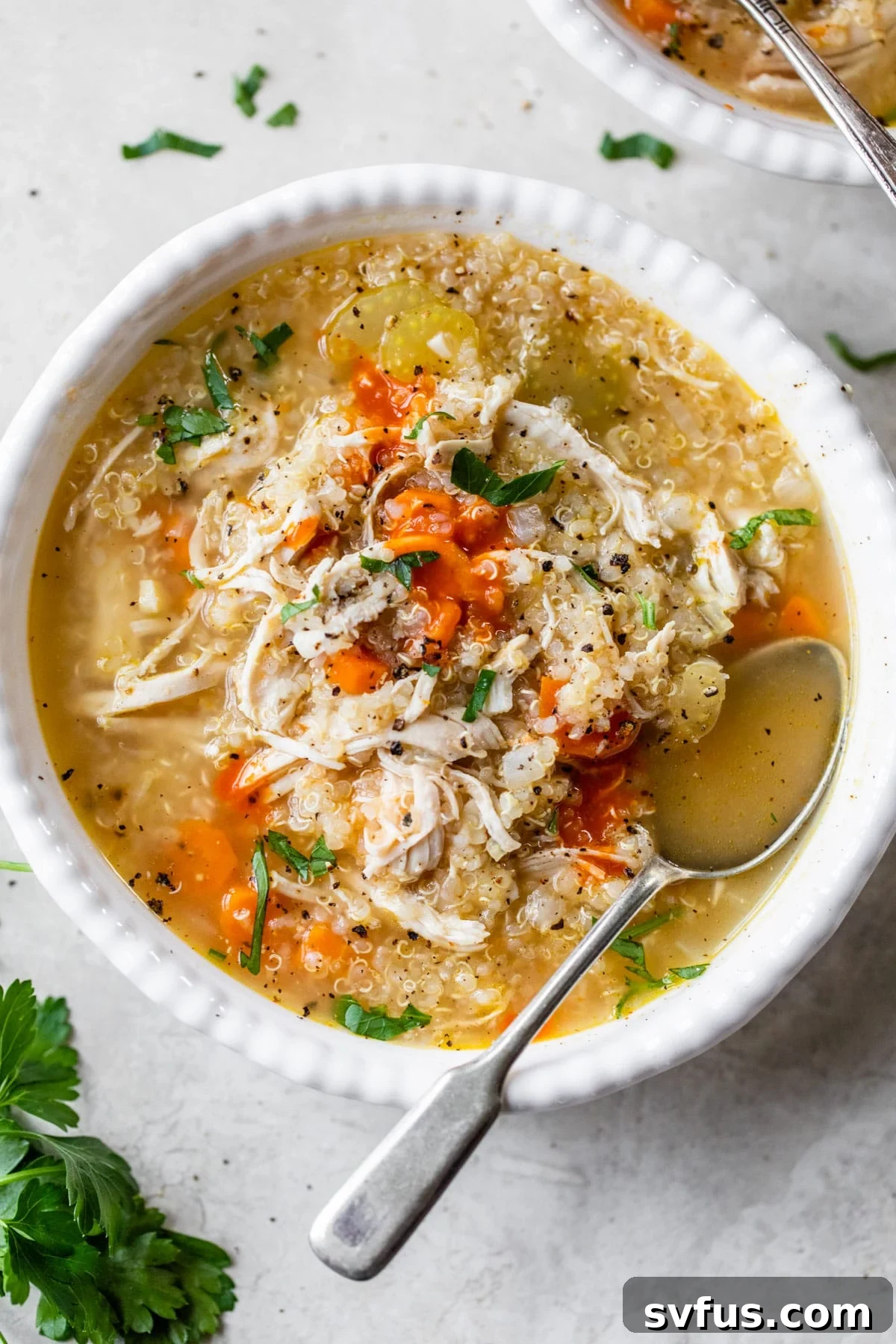 A bowl of Chicken Quinoa Soup topped with shredded chicken, parsley, and a drizzle of hot sauce.