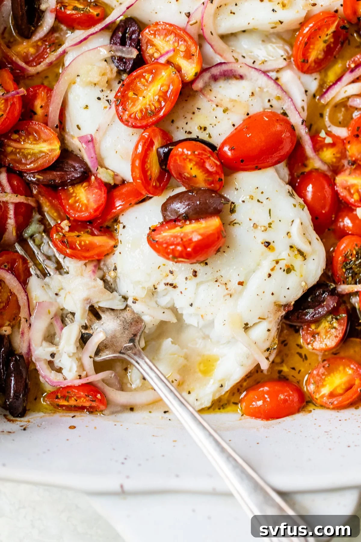 Flaky baked cod in a baking dish with tomatoes, onion and olives, ready to be served.