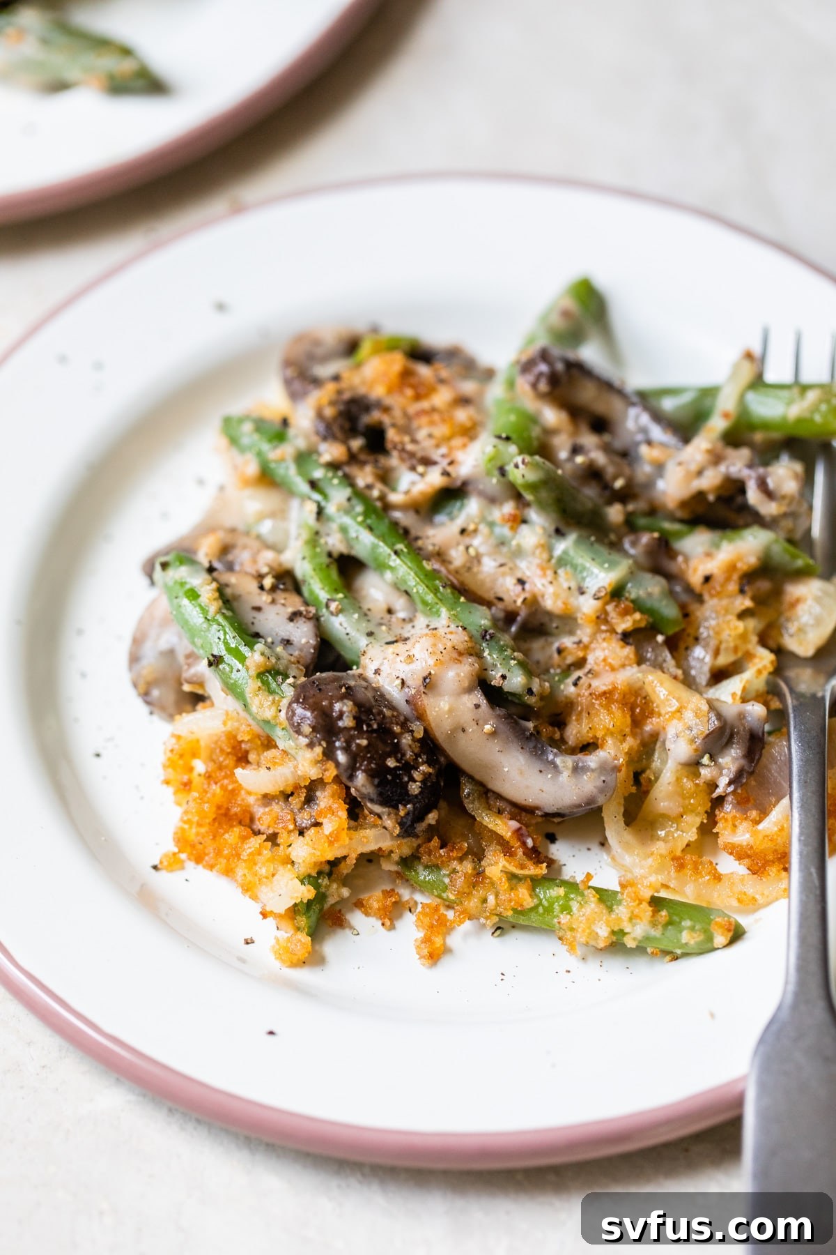 A serving of vegan green bean casserole with mushrooms and crispy onions on a plate with a fork.
