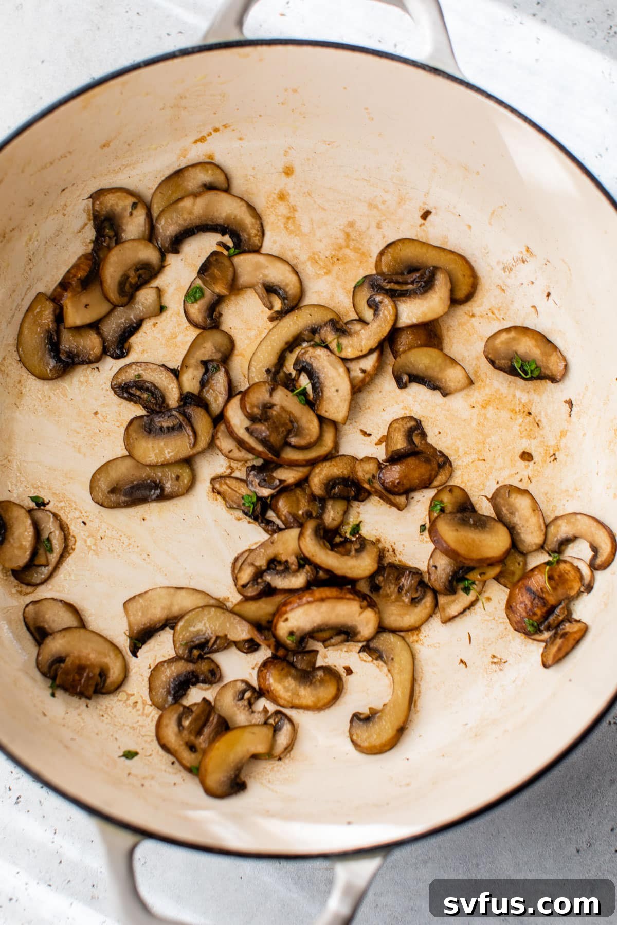 Mushrooms sautéing in a Dutch oven with thyme and salt, preparing for the cheese sauce