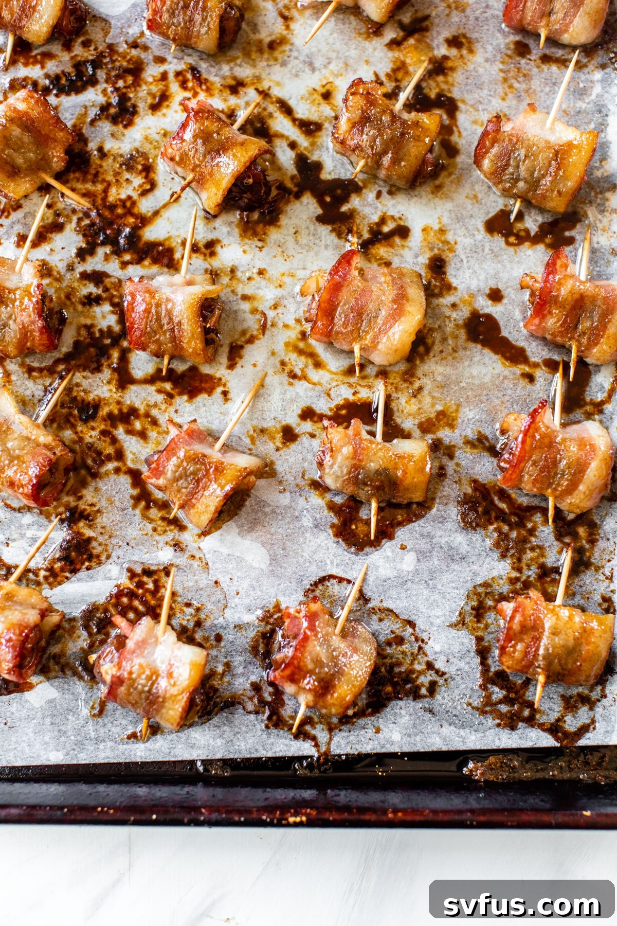 Bacon-wrapped dates arranged neatly on a baking sheet lined with parchment paper, ready for baking.