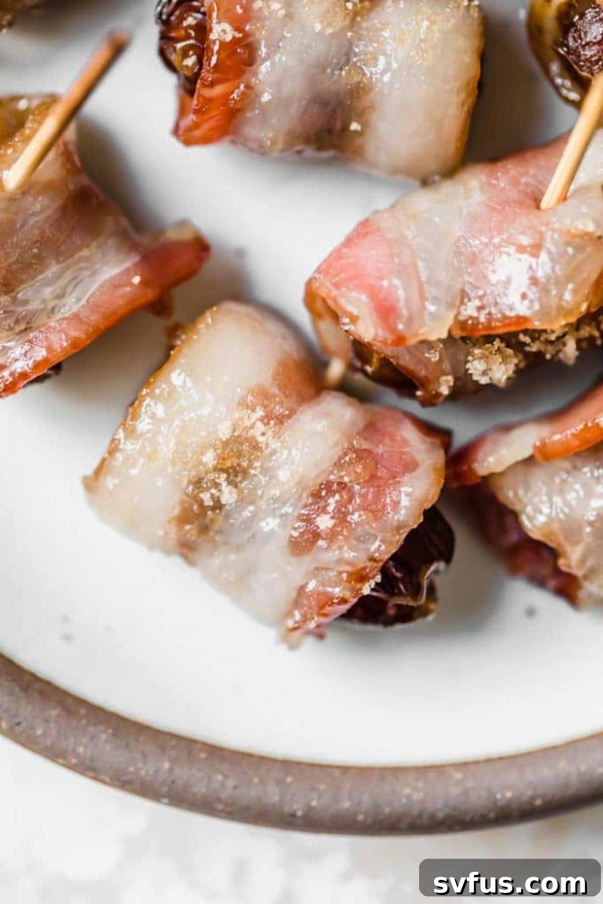A single, perfectly baked bacon-wrapped date on a white plate, showcasing its crispy bacon and caramelized exterior.