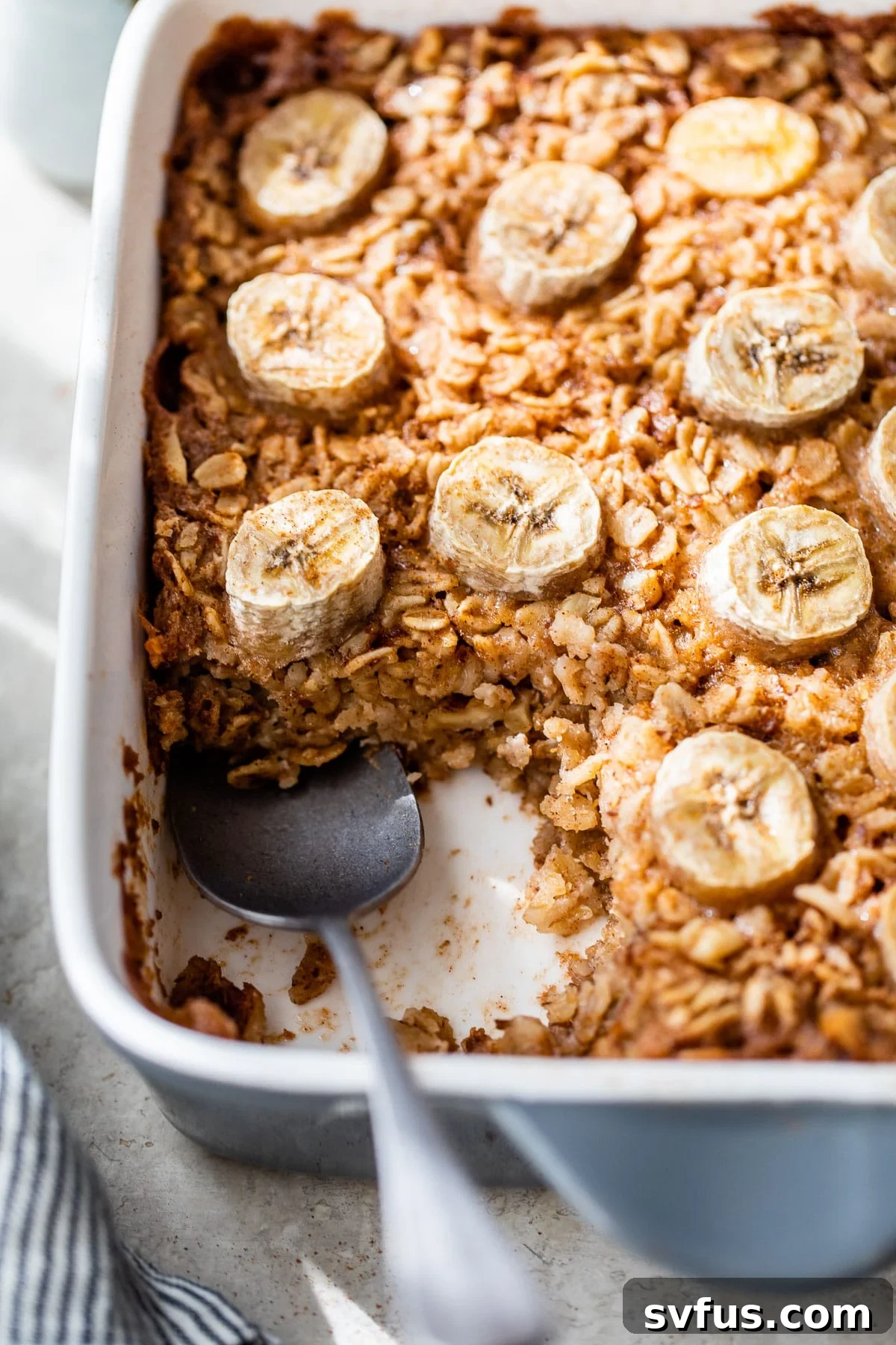 A golden-brown baked banana oatmeal in a baking dish, generously topped with perfectly sliced ripe bananas, hinting at its warm, comforting essence.
