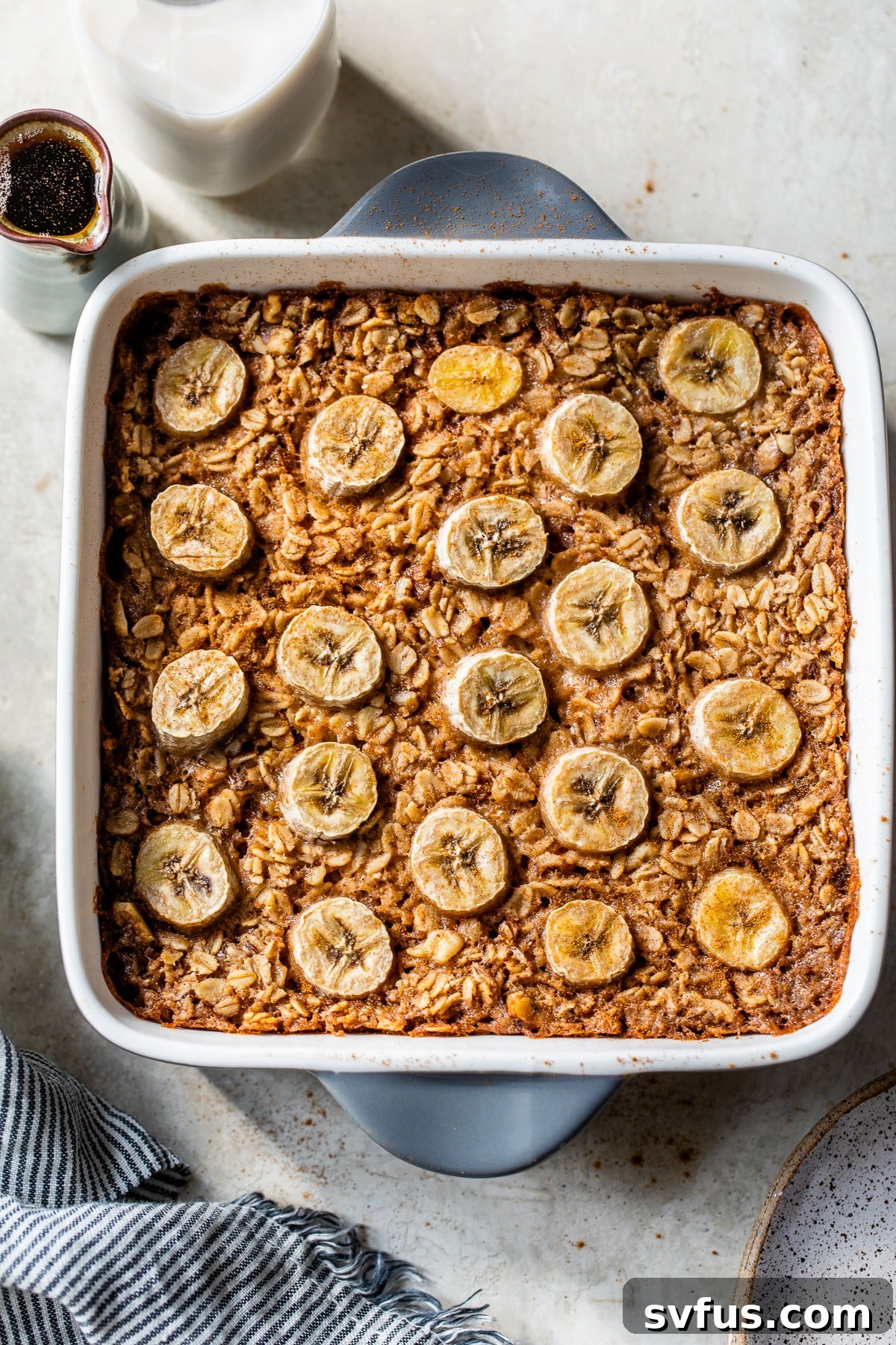 A vibrant close-up of baked oatmeal with golden-brown edges and sliced bananas on top, still warm and inviting in a square baking dish, ready to be served.