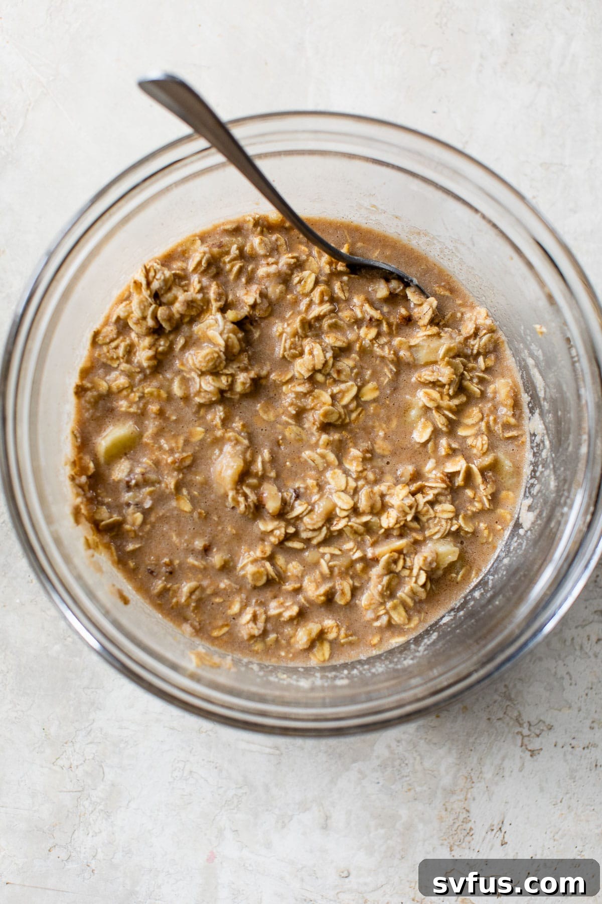 A close-up shot of a glass bowl holding the combined wet and dry ingredients for baked oatmeal, featuring oats soaking in milk and banana, ready for baking.