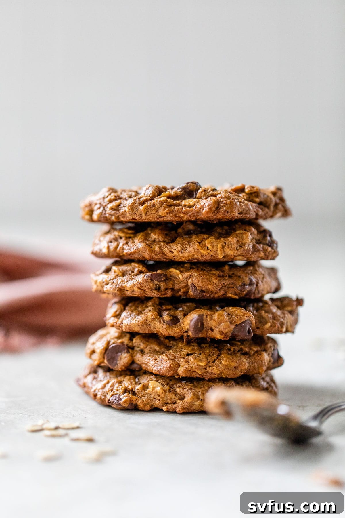 A beautifully arranged stack of freshly baked almond butter oatmeal cookies with chocolate chips, positioned next to a spoon laden with creamy almond butter, highlighting the key ingredient.