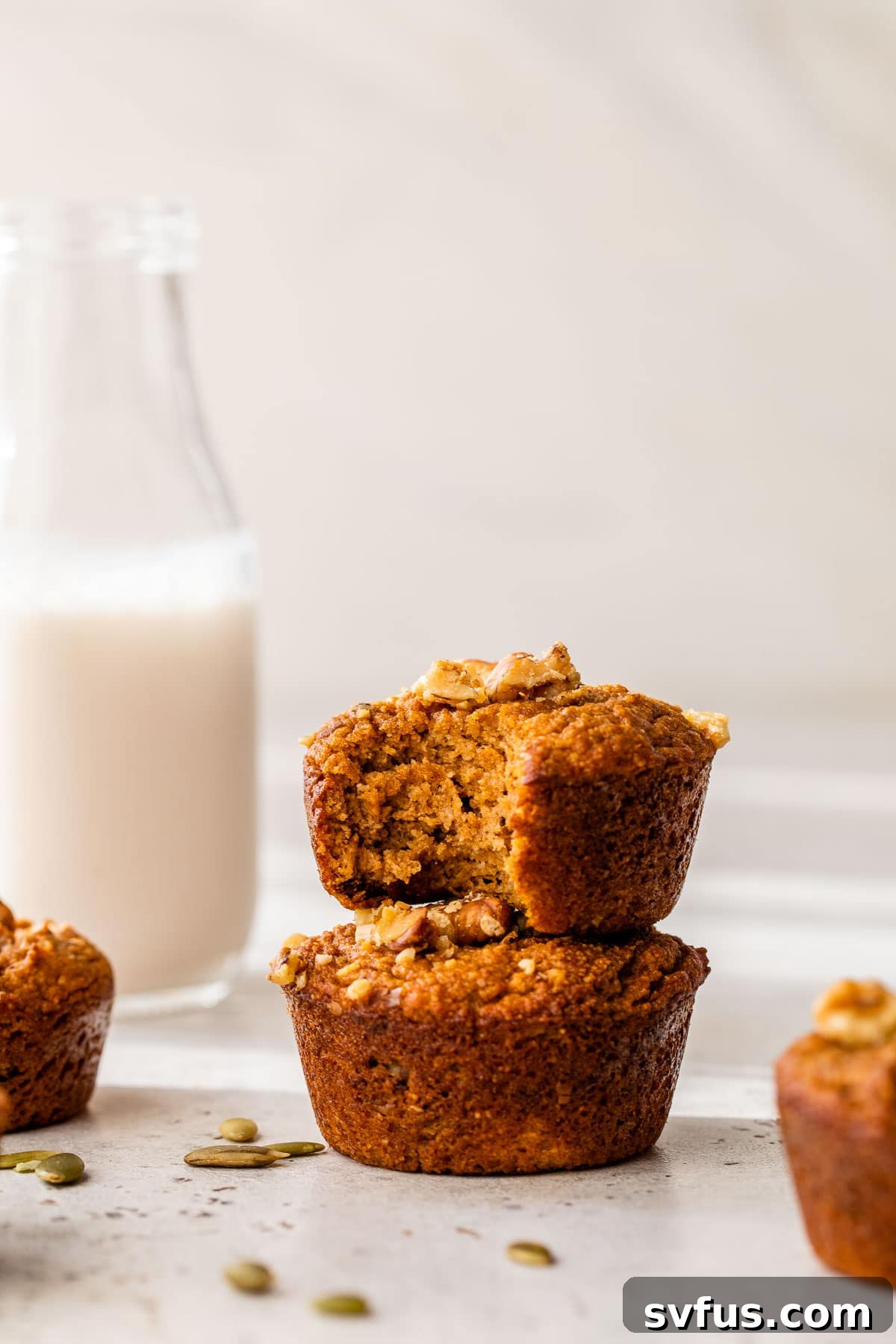 Two golden-brown Paleo Pumpkin Muffins, stacked elegantly beside a tall glass of milk, inviting a cozy fall snack.