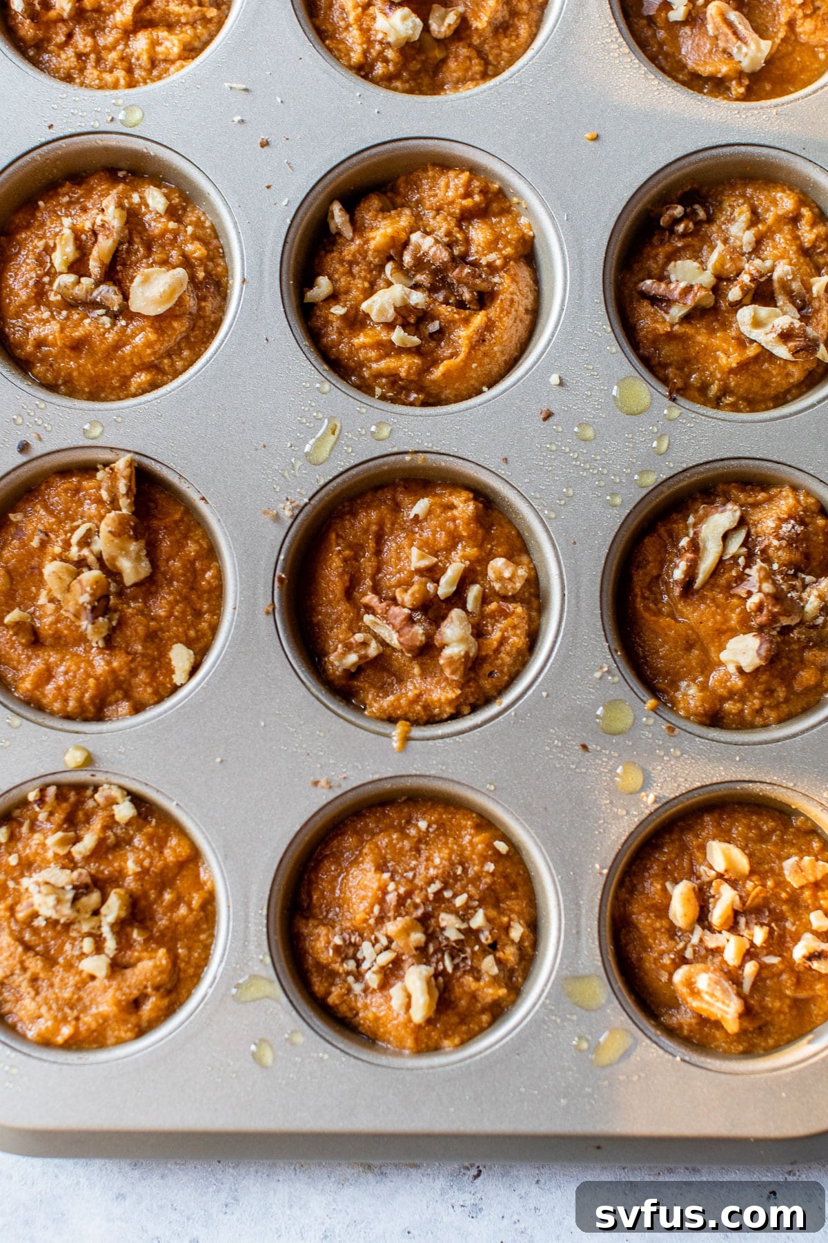 Rows of raw pumpkin muffin batter, neatly scooped into a muffin tin, patiently awaiting their transformation in the oven.