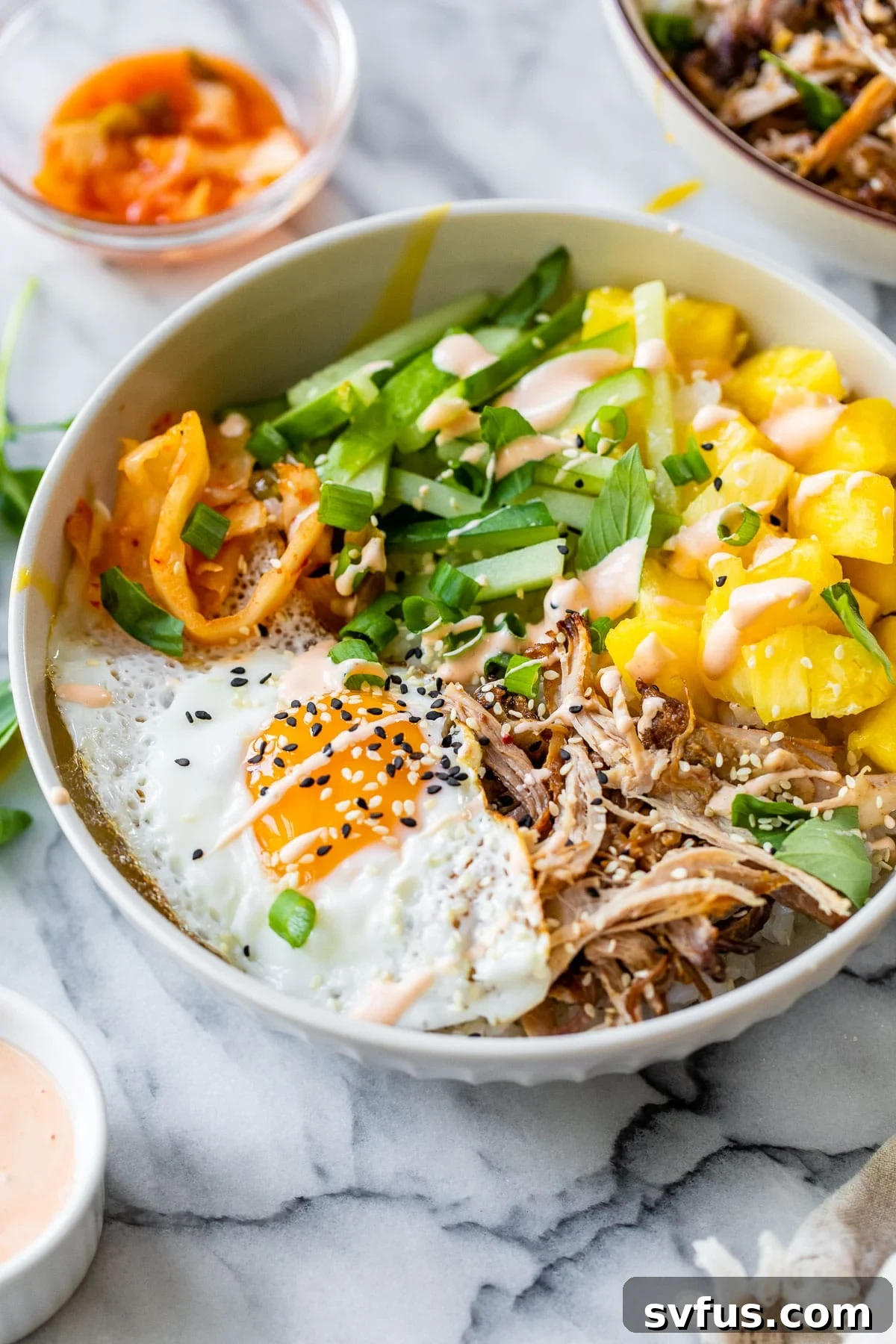 A beautifully assembled Hawaiian Bibimbap bowl featuring rice, pulled pork, fresh pineapple, cucumber, kimchi, and a fried egg