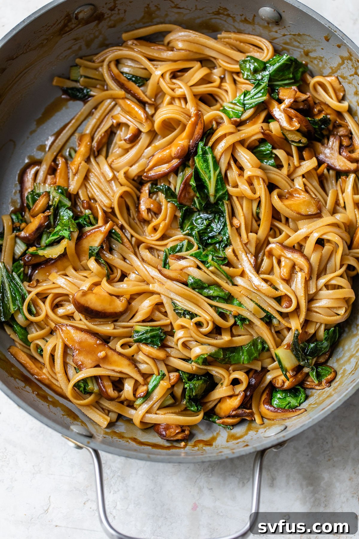 A vibrant skillet overflowing with long teriyaki noodles, mushrooms, and bok choy, coated in a glossy sauce.
