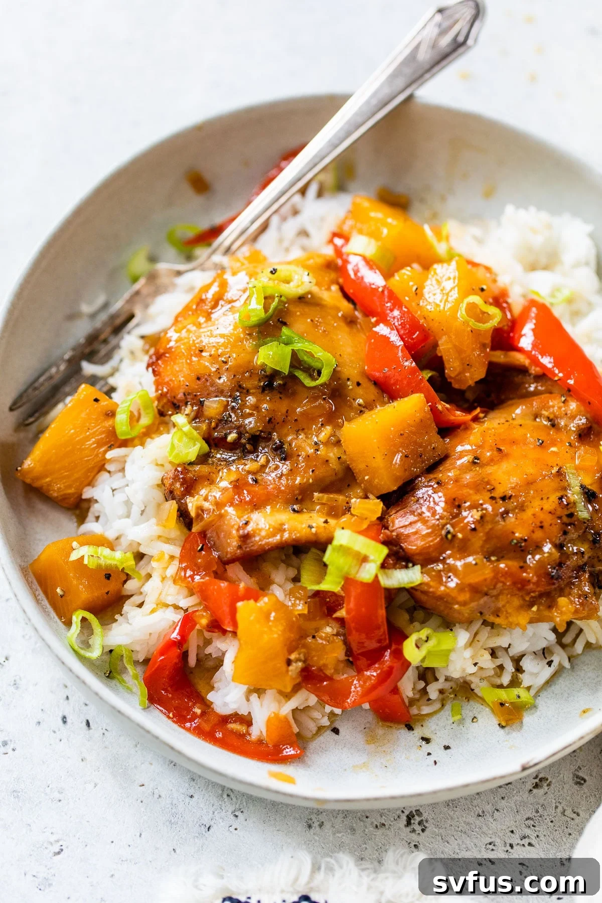 A vibrant bowl of Crockpot Hawaiian Chicken served over white rice, garnished with fresh green onions.