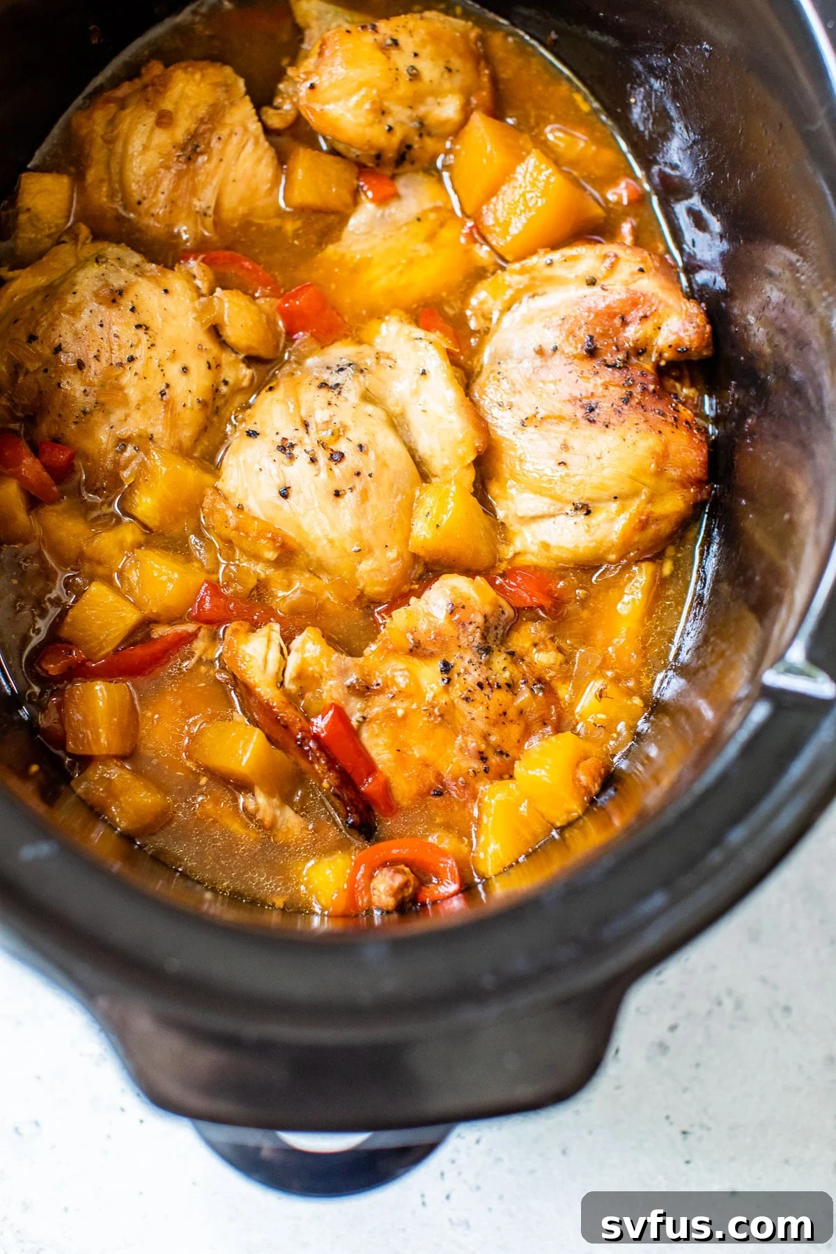 A slow cooker filled with cooked Hawaiian chicken, pineapple, and bell peppers, ready to be served.