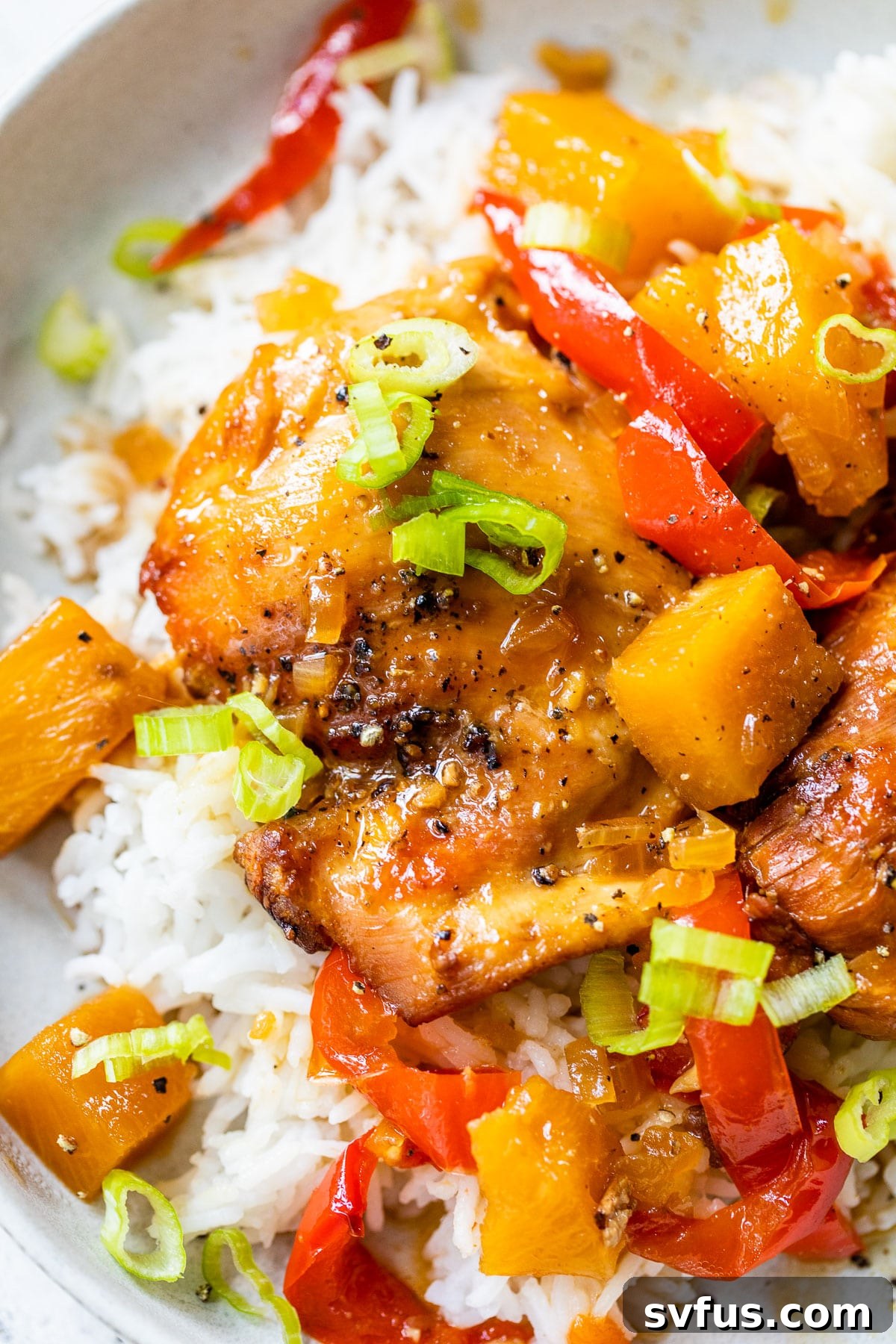 A close-up shot of a perfectly cooked chicken thigh with red bell peppers and diced pineapple, coated in a sticky Hawaiian sauce.