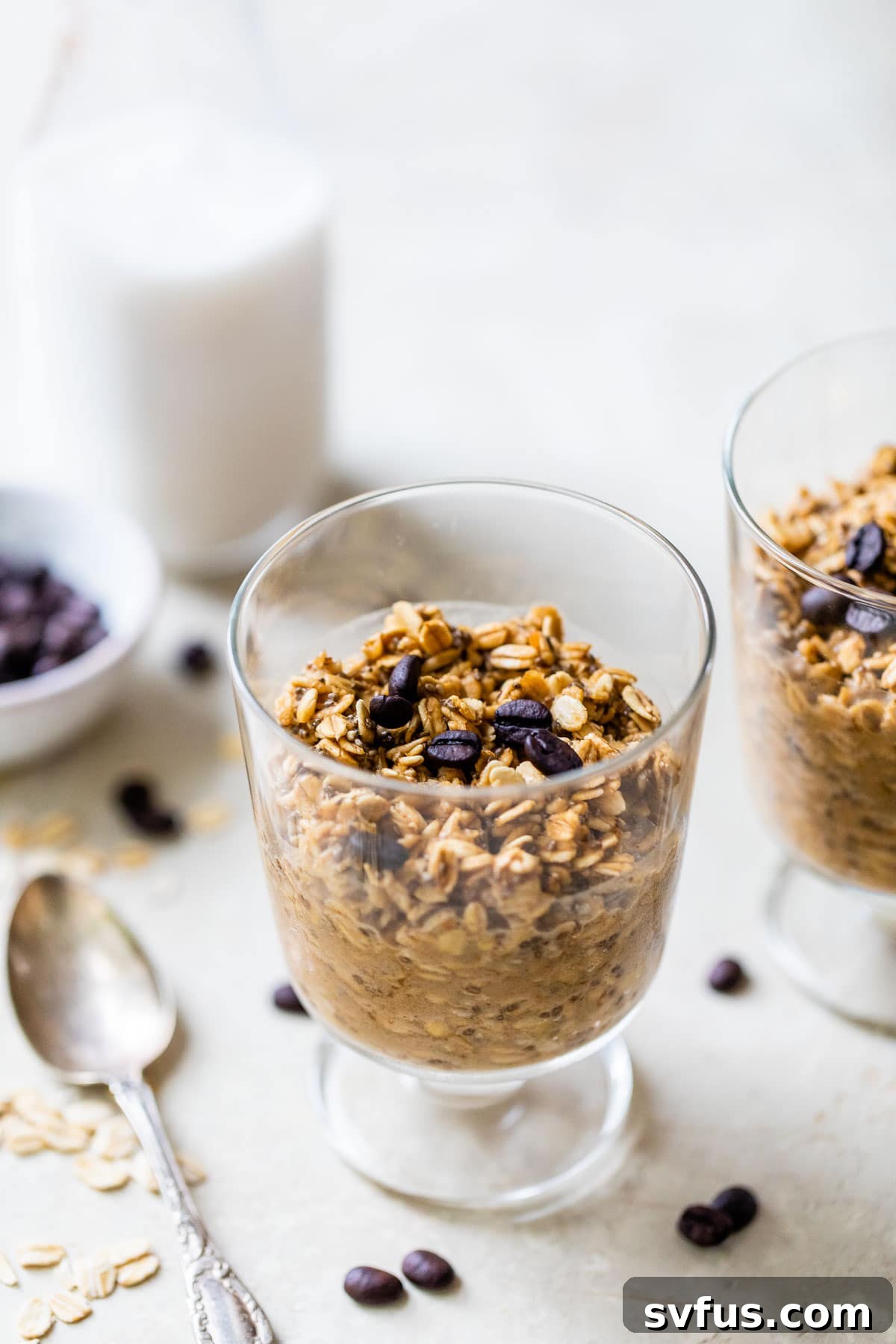 A glass jar filled with coffee overnight oats, topped with a few whole coffee beans, against a soft background.