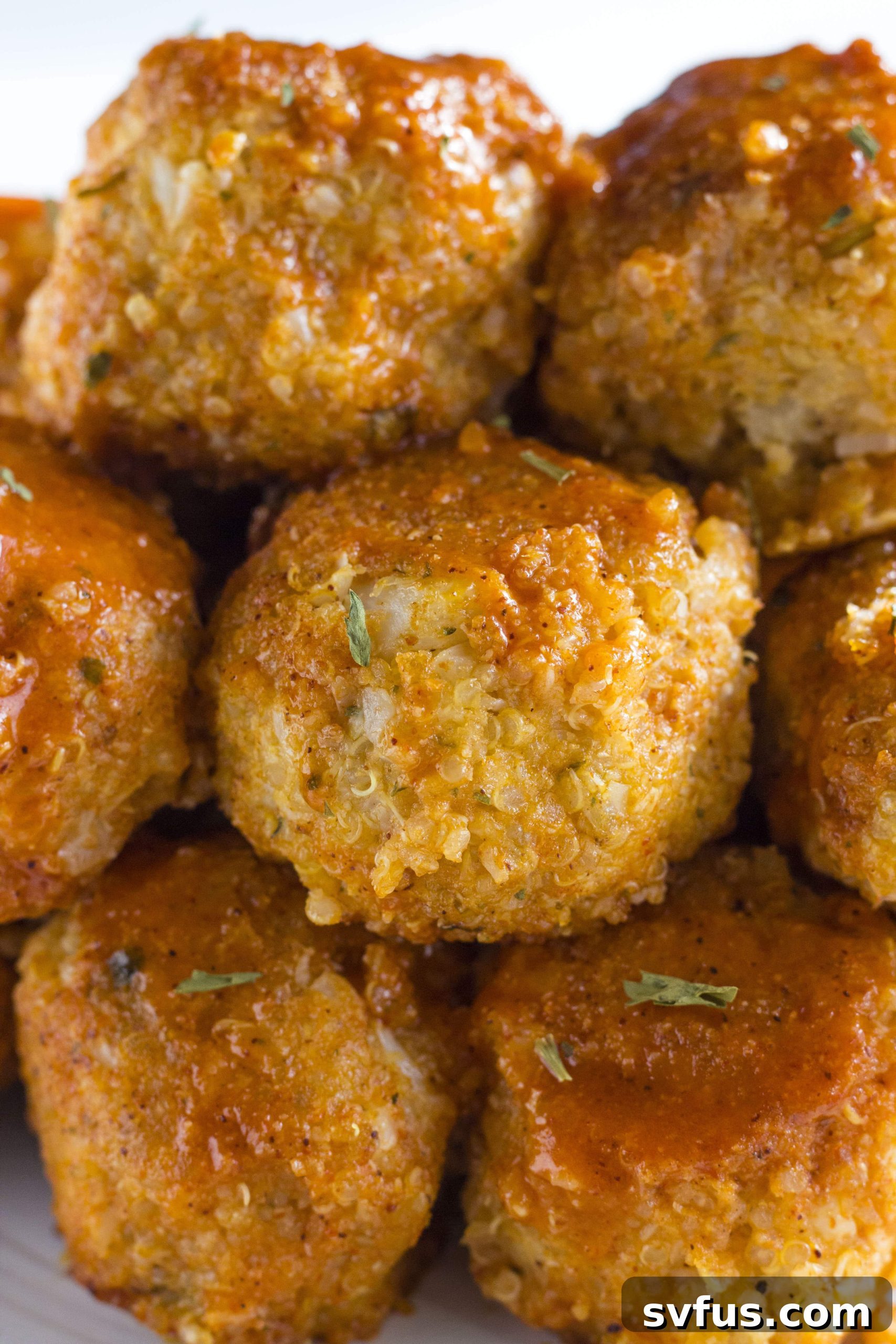 Delicious Buffalo Cauliflower Quinoa Meatballs coated in sauce on a skillet.