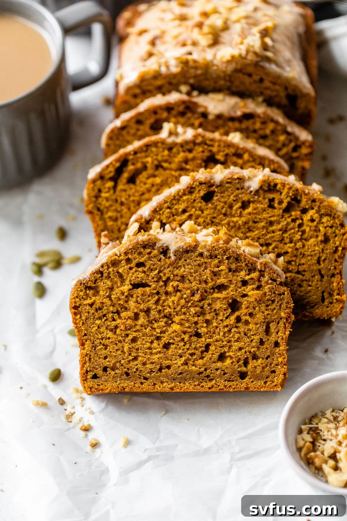 sliced pumpkin bread on parchment paper beside a mug of coffee