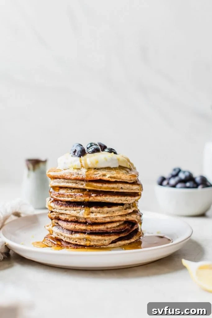 A stack of fluffy blueberry chia seed pancakes topped with Greek yogurt, lemon zest, fresh blueberries, and a drizzle of maple syrup