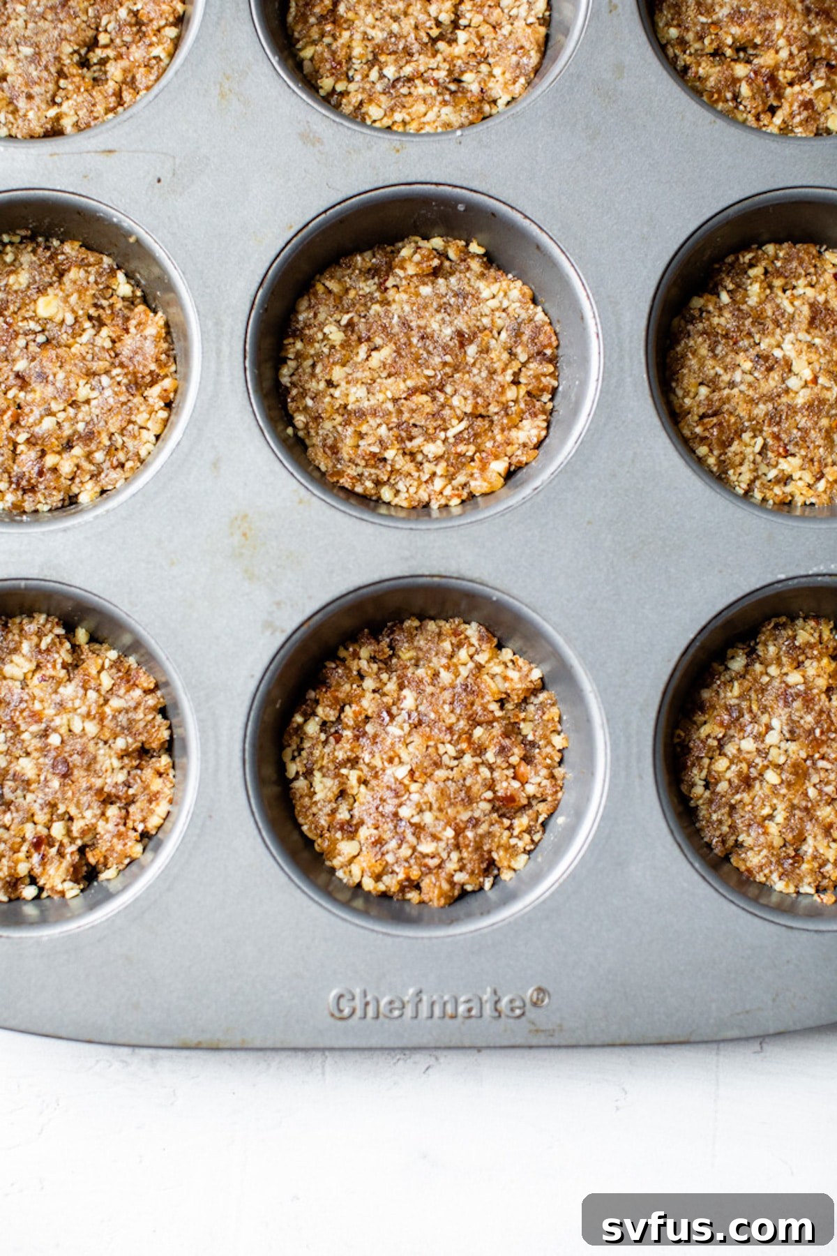 The vegan pie crust mixture pressed firmly into the bottom of a greased 12-cup muffin tin, ready for freezing.
