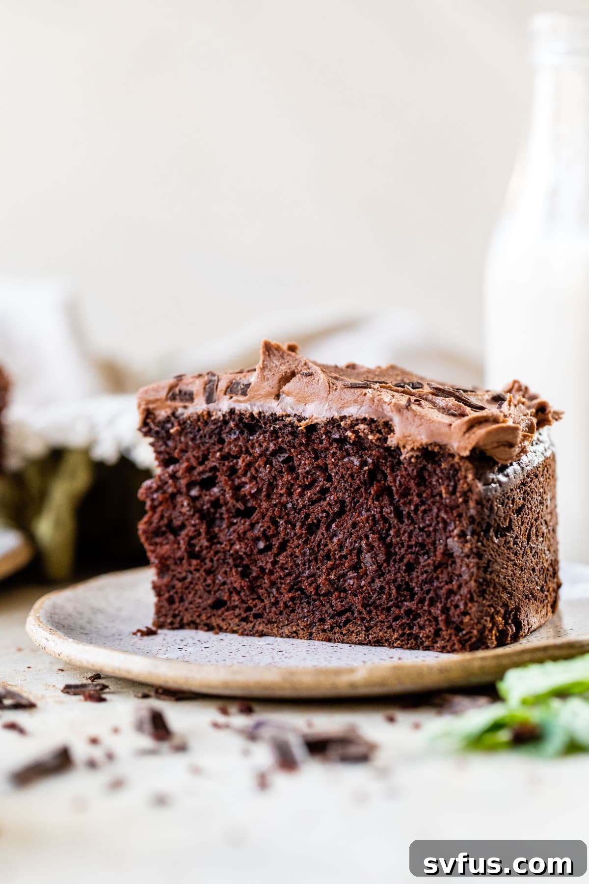 A perfectly sliced piece of chocolate mint cake, revealing its tender crumb, sits invitingly on a white plate next to a tall glass of almond milk.