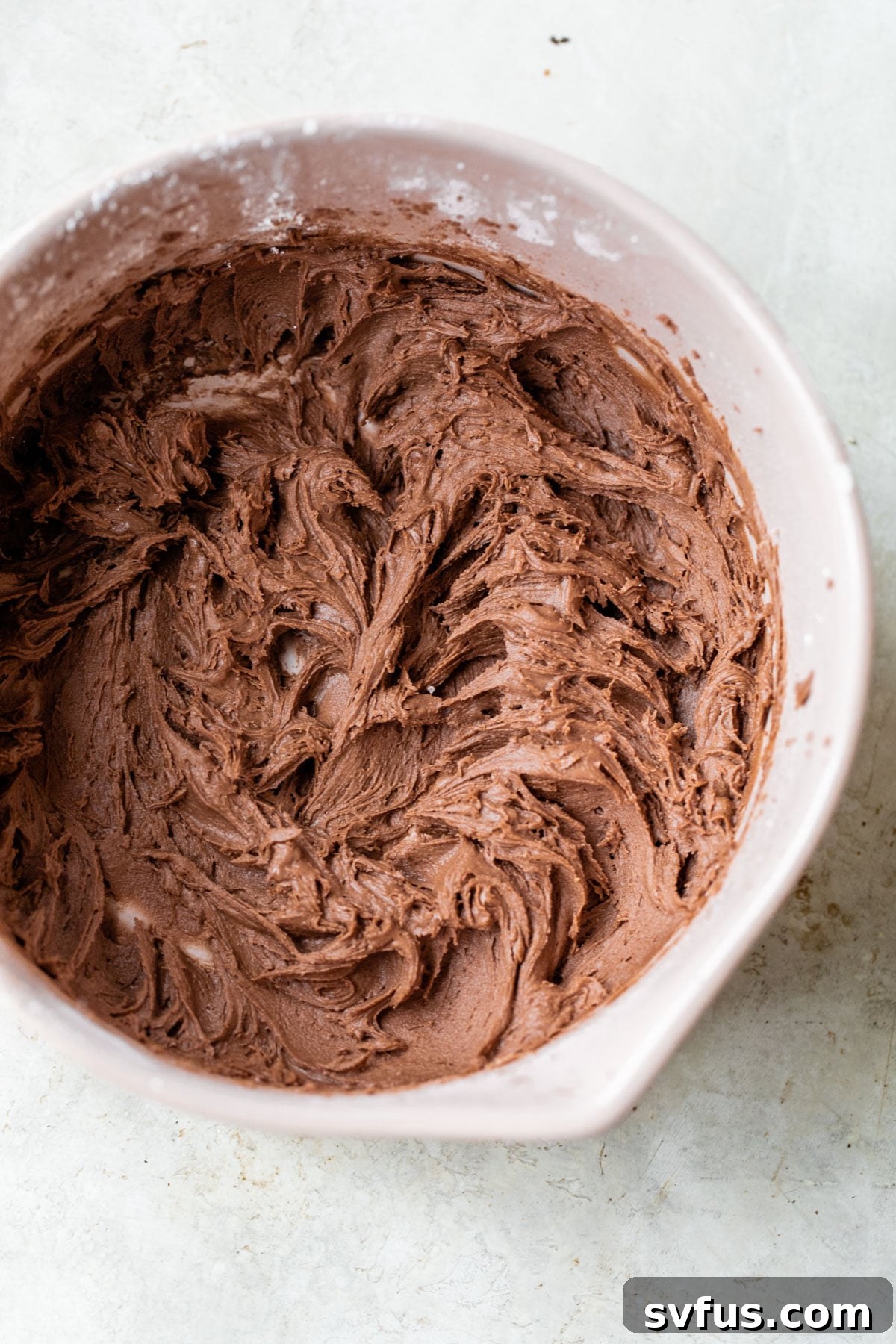 A vibrant pink mixing bowl filled with smooth, rich chocolate buttercream icing, ready to be spread onto a cake.