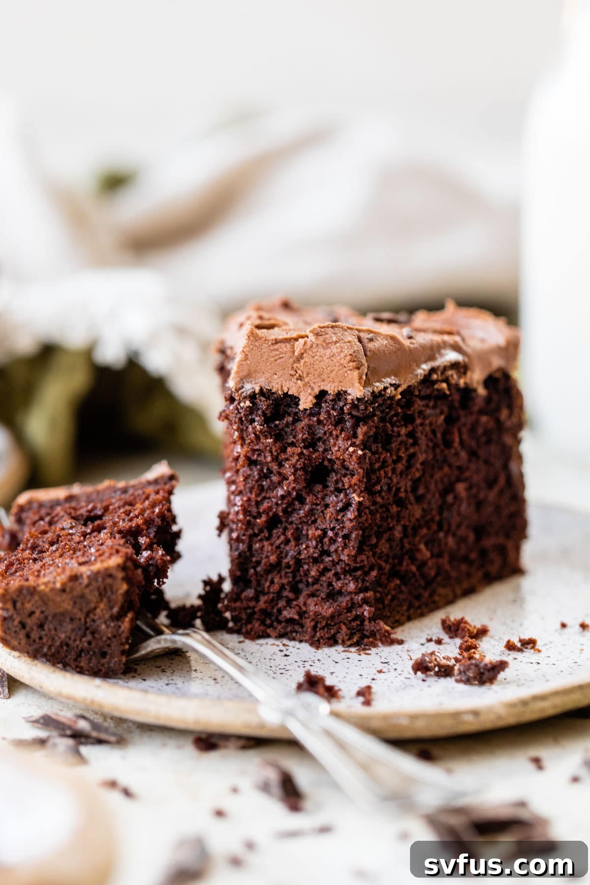 A close-up of a slice of moist chocolate mint cake on a white plate, with a bite playfully taken out, highlighting its delicious texture.