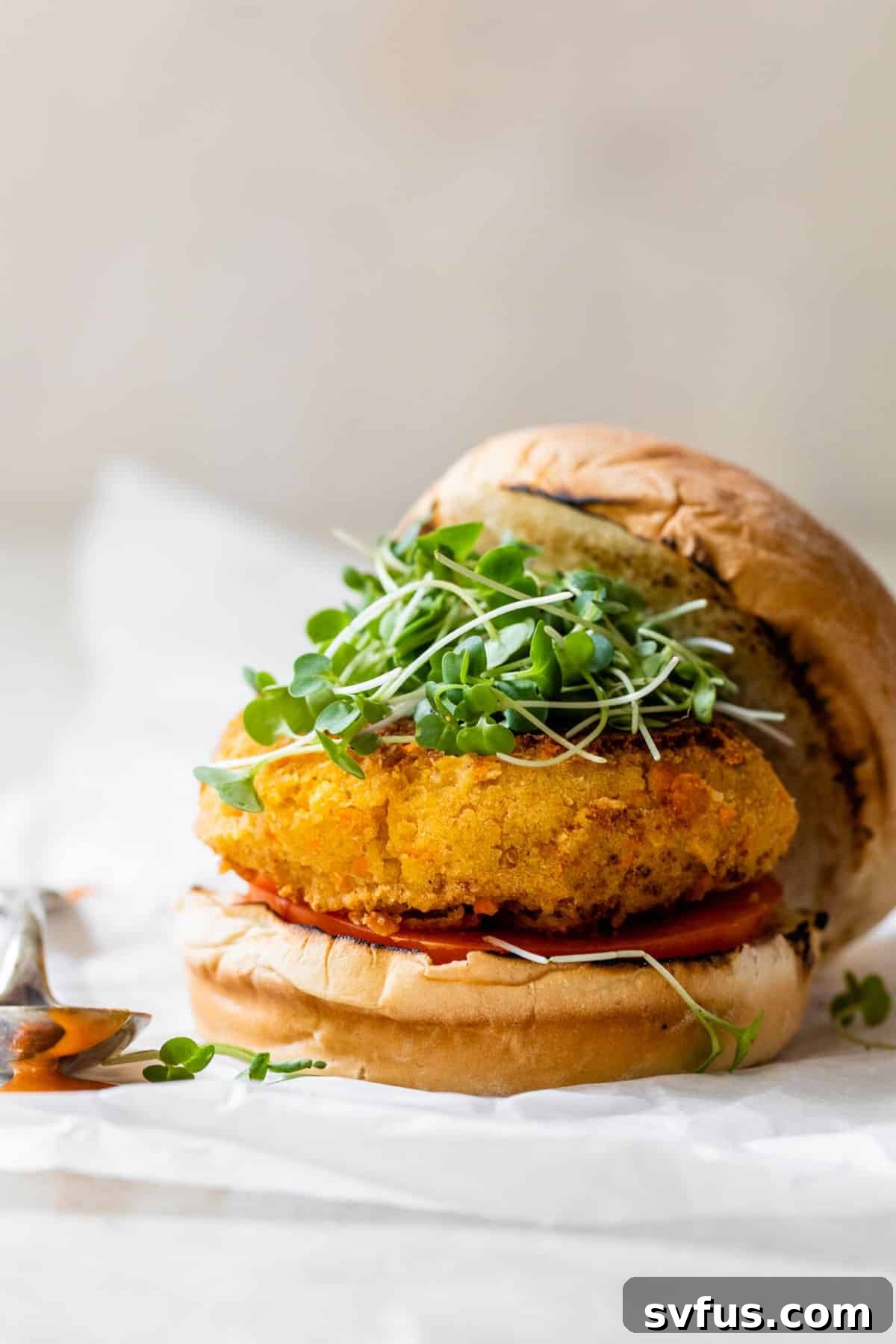 A perfectly golden brown Buffalo Chickpea Burger on a toasted bun with fresh microgreens, ready to be enjoyed.