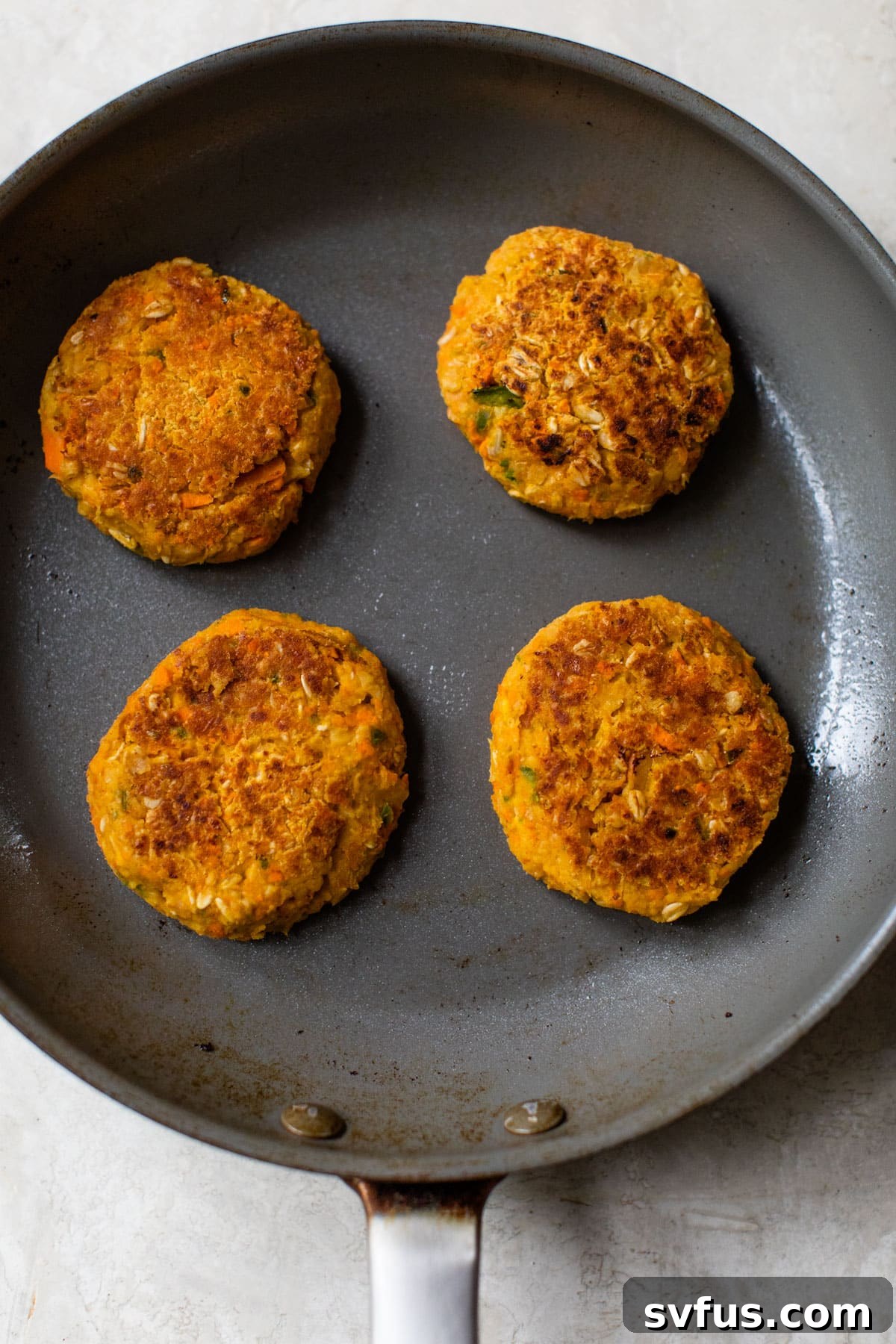 Several Buffalo Chickpea Burgers sizzling in a hot skillet, achieving a perfect golden-brown crust.