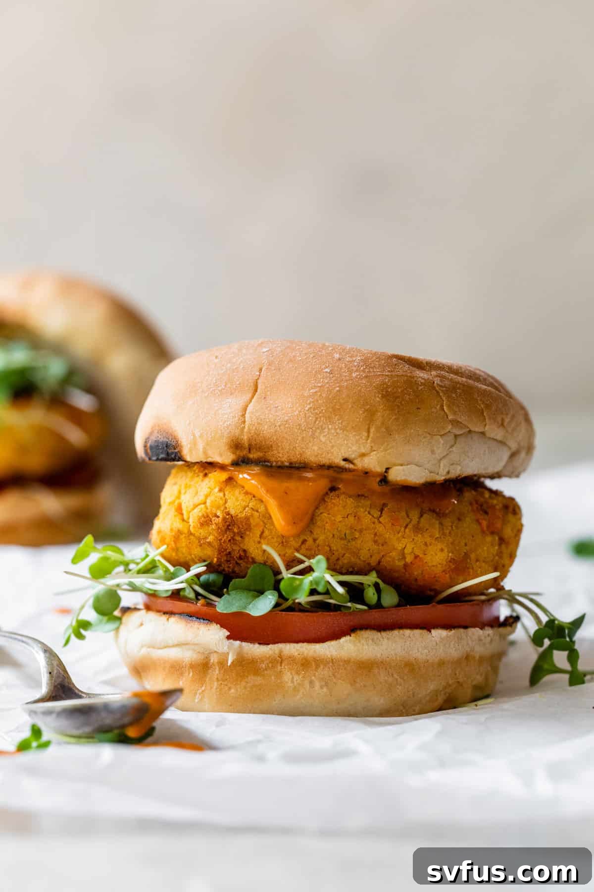 A Buffalo Chickpea Burger nestled in a bun, wrapped in parchment paper, showcasing its appealing texture and readiness to be eaten.