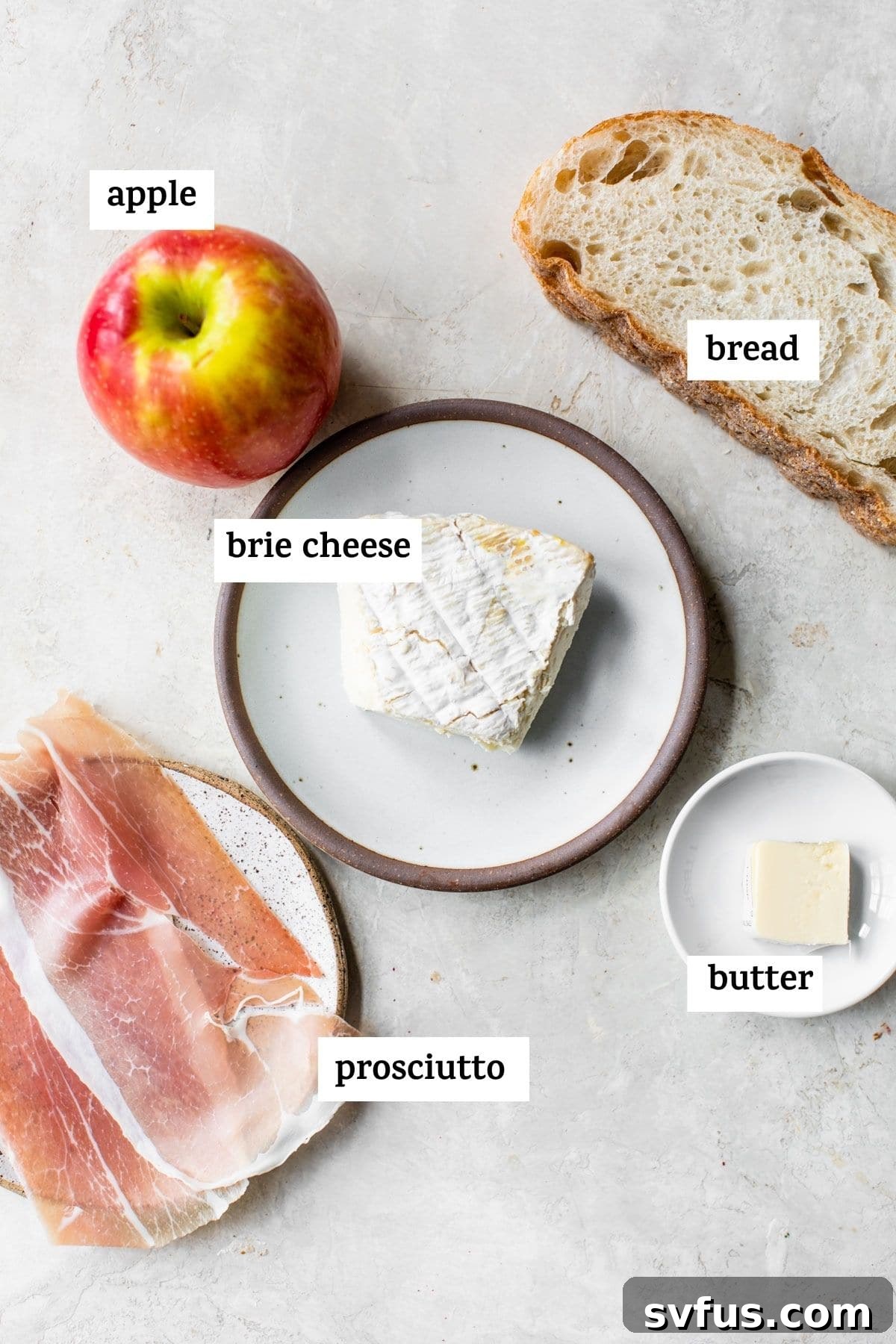 Key ingredients laid out for making the sandwich, including a block of brie cheese and a fresh apple.