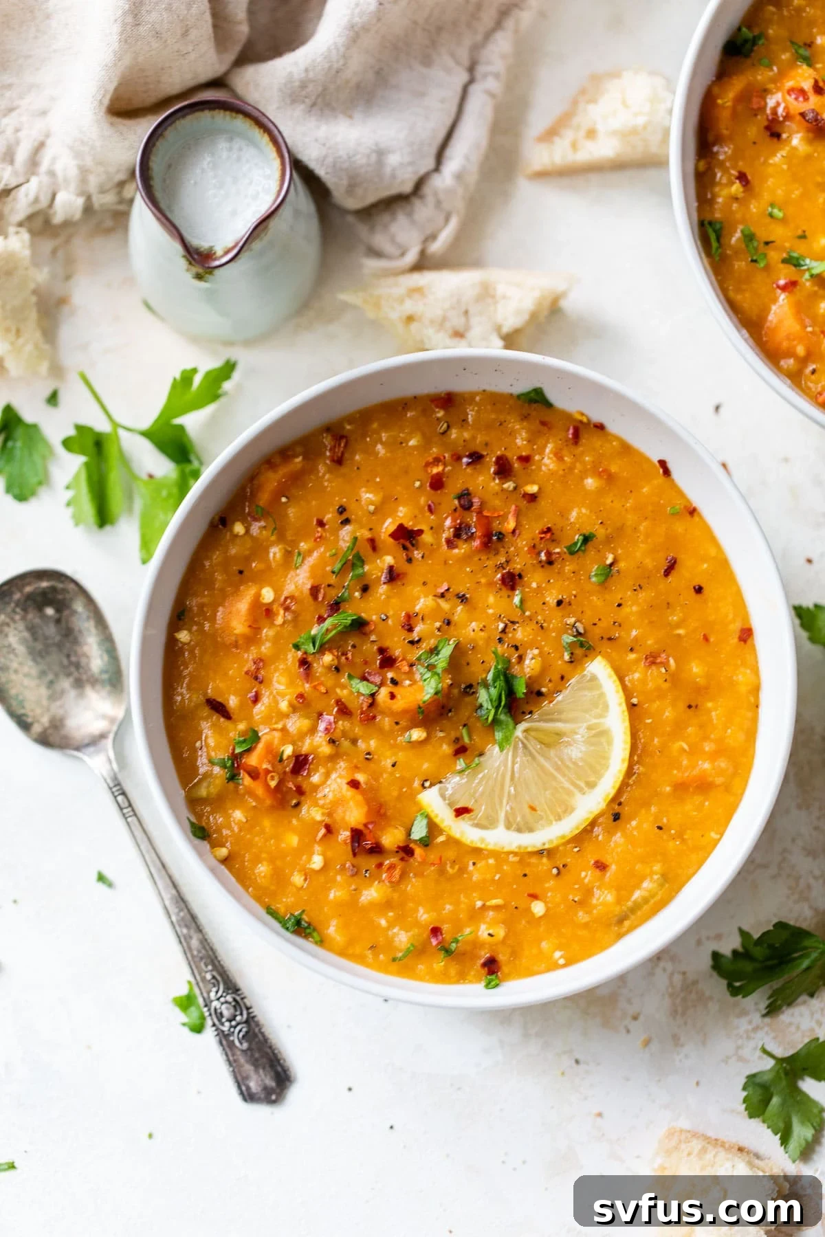 A vibrant bowl of red lentil soup, artfully garnished with a delicate lemon wedge, highlighting its rich color and inviting texture.
