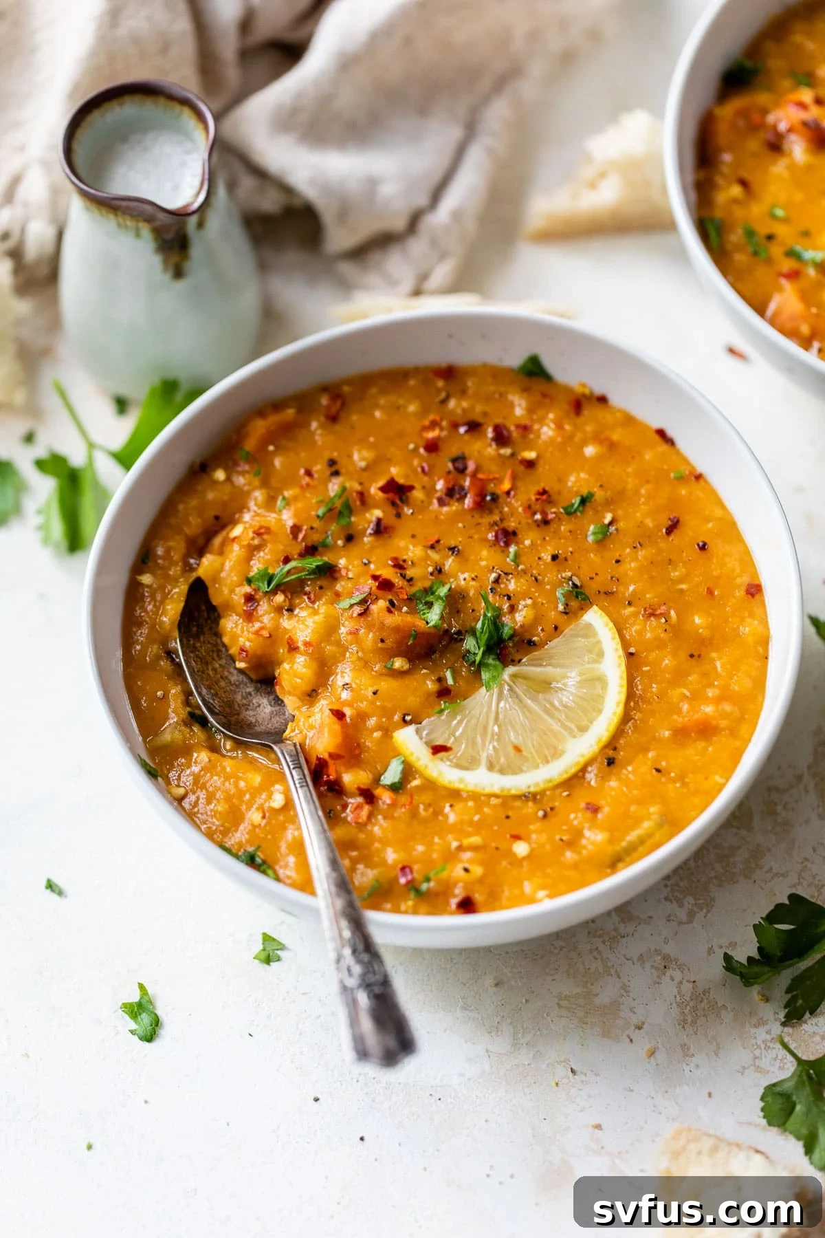 A beautifully presented bowl of creamy red lentil soup, accompanied by a spoon and a slice of lemon, ready to be enjoyed.