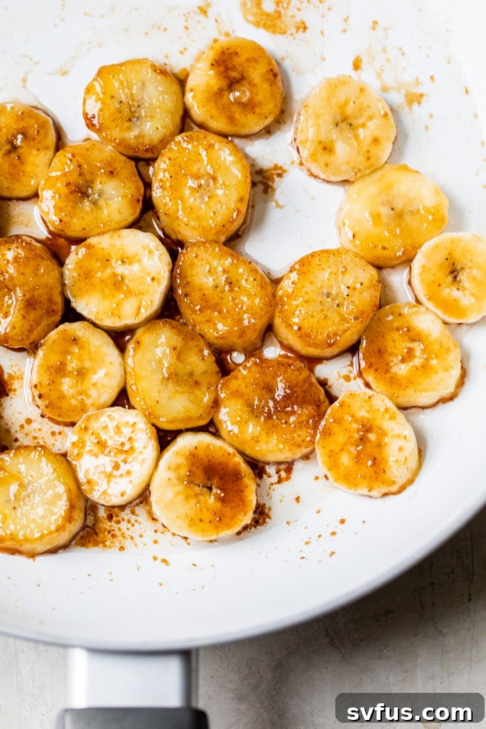 Sliced bananas cooking in a skillet with coconut oil and sprinkled coconut sugar, beginning to caramelize and turn golden.