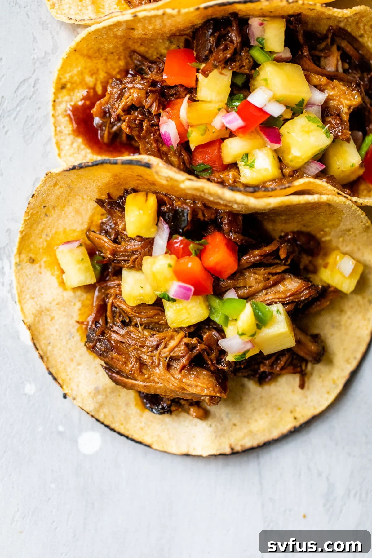 two tacos on a table topped with shredded pork and salsa