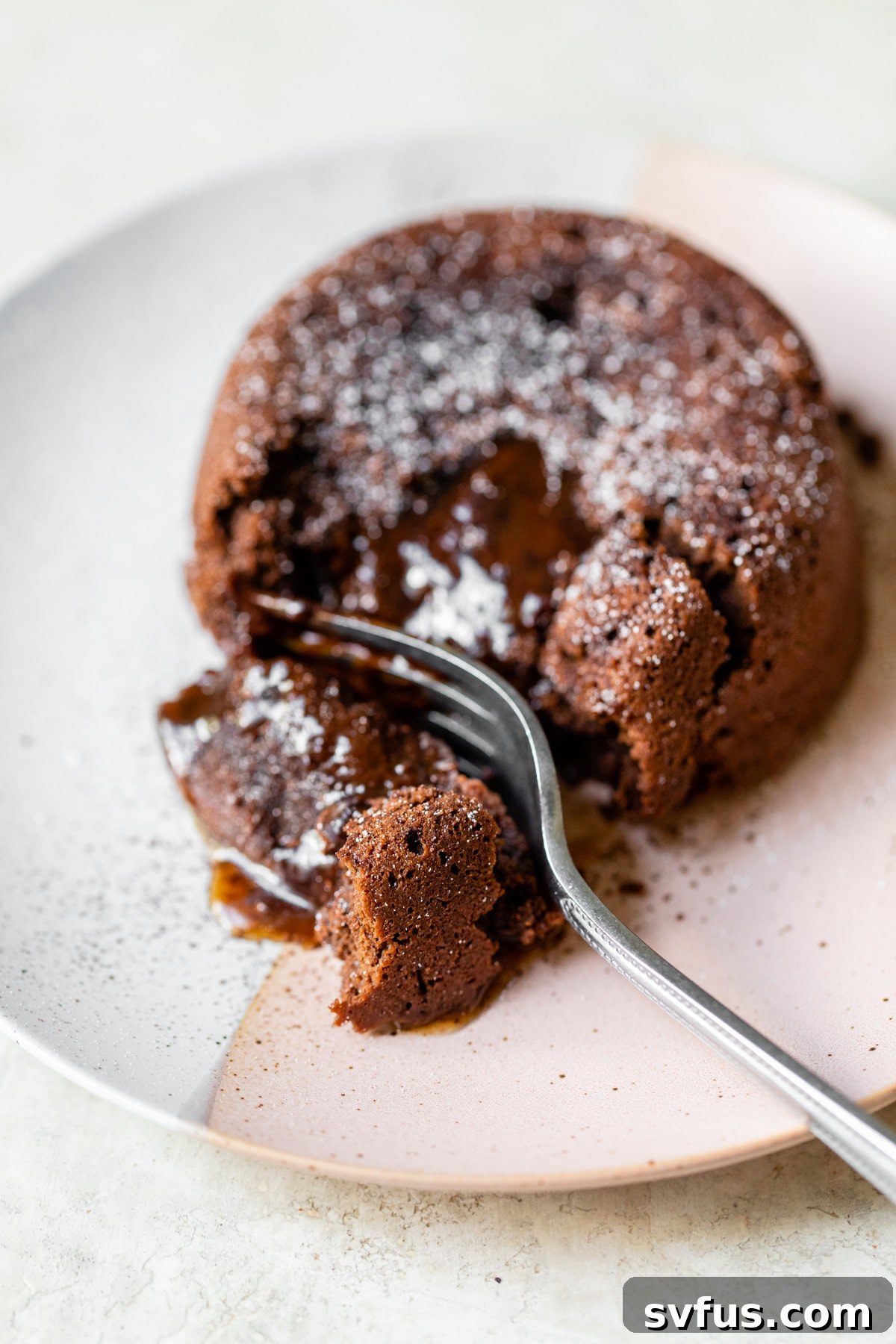 A beautifully presented chocolate caramel lava cake, perfectly unmolded on a white plate, with a light dusting of powdered sugar. The cake exhibits its soft, slightly molten center with a hint of caramel.