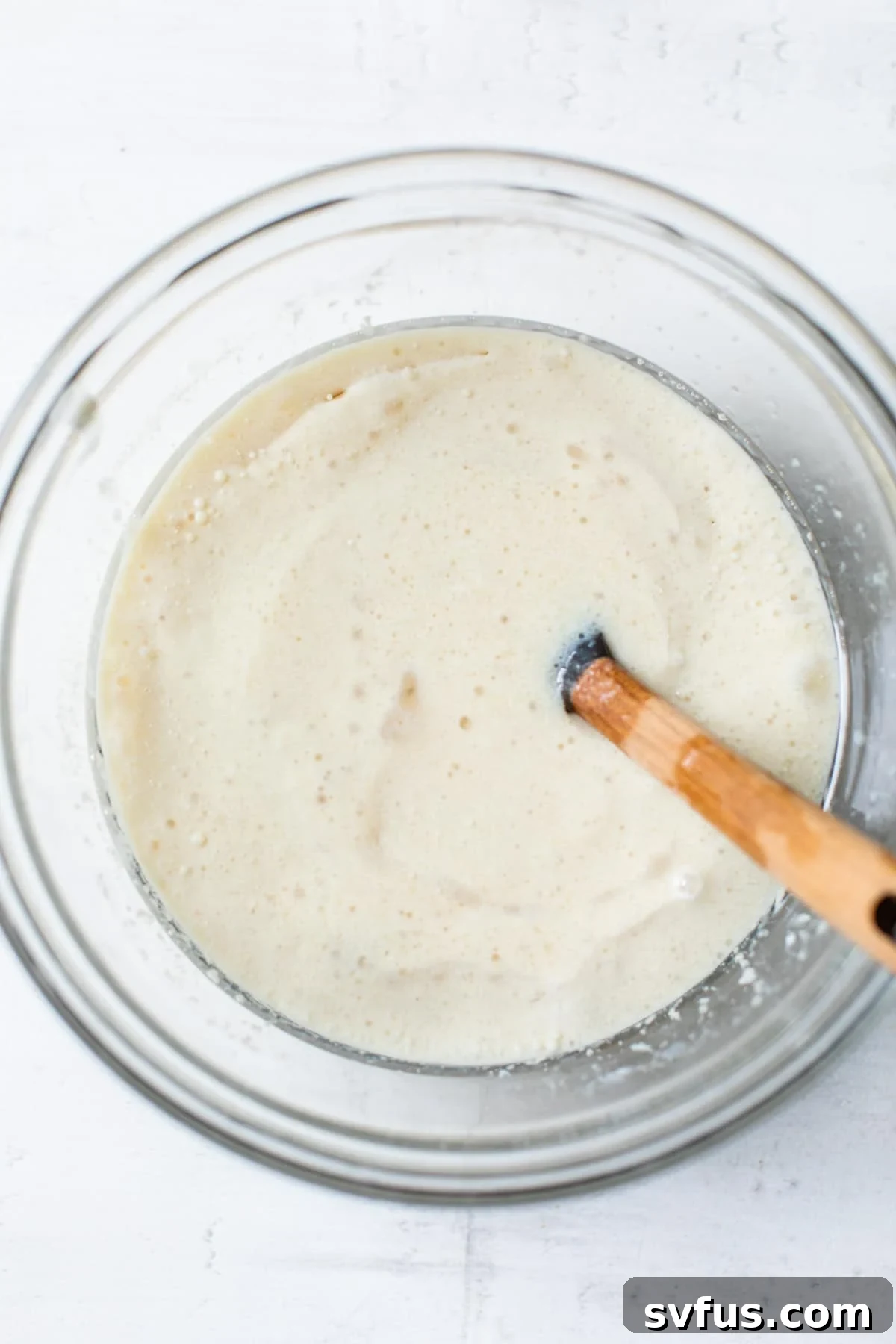 A bowl filled with wet cake ingredients like milk, applesauce, and vanilla extract, being whisked.