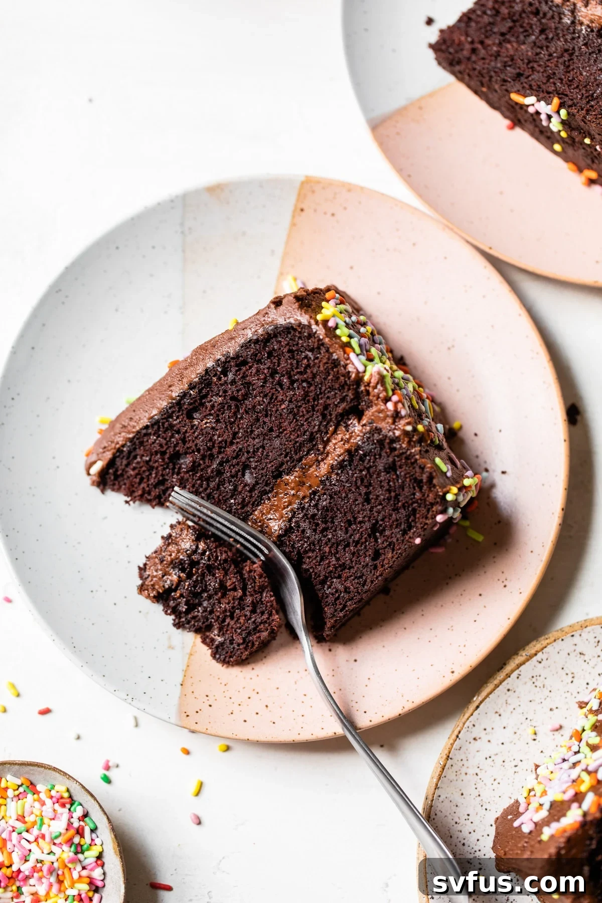 A close-up shot of a single slice of rich chocolate vegan birthday cake on a white plate, showcasing its moist texture and creamy frosting.