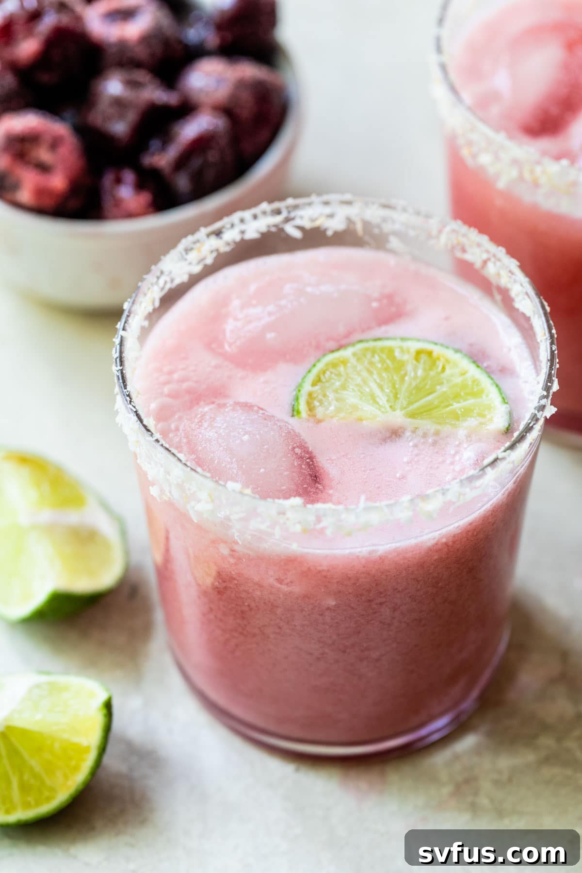 A beautiful pink coconut cherry margarita garnished with toasted coconut flakes and a lime slice
