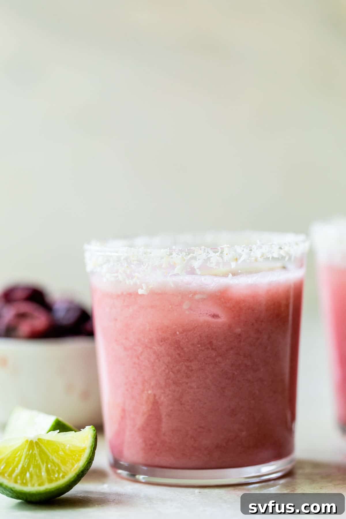 A vibrant cherry cocktail next to a bowl of fresh cherries and a lime wedge