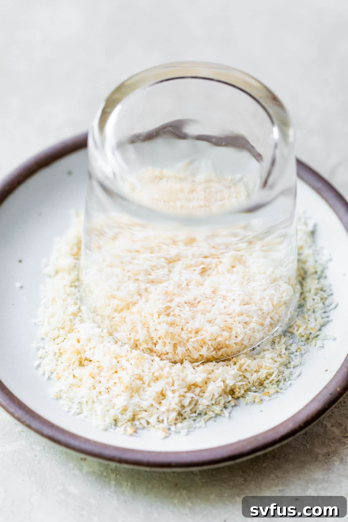 A cocktail glass being rimmed with toasted shredded coconut