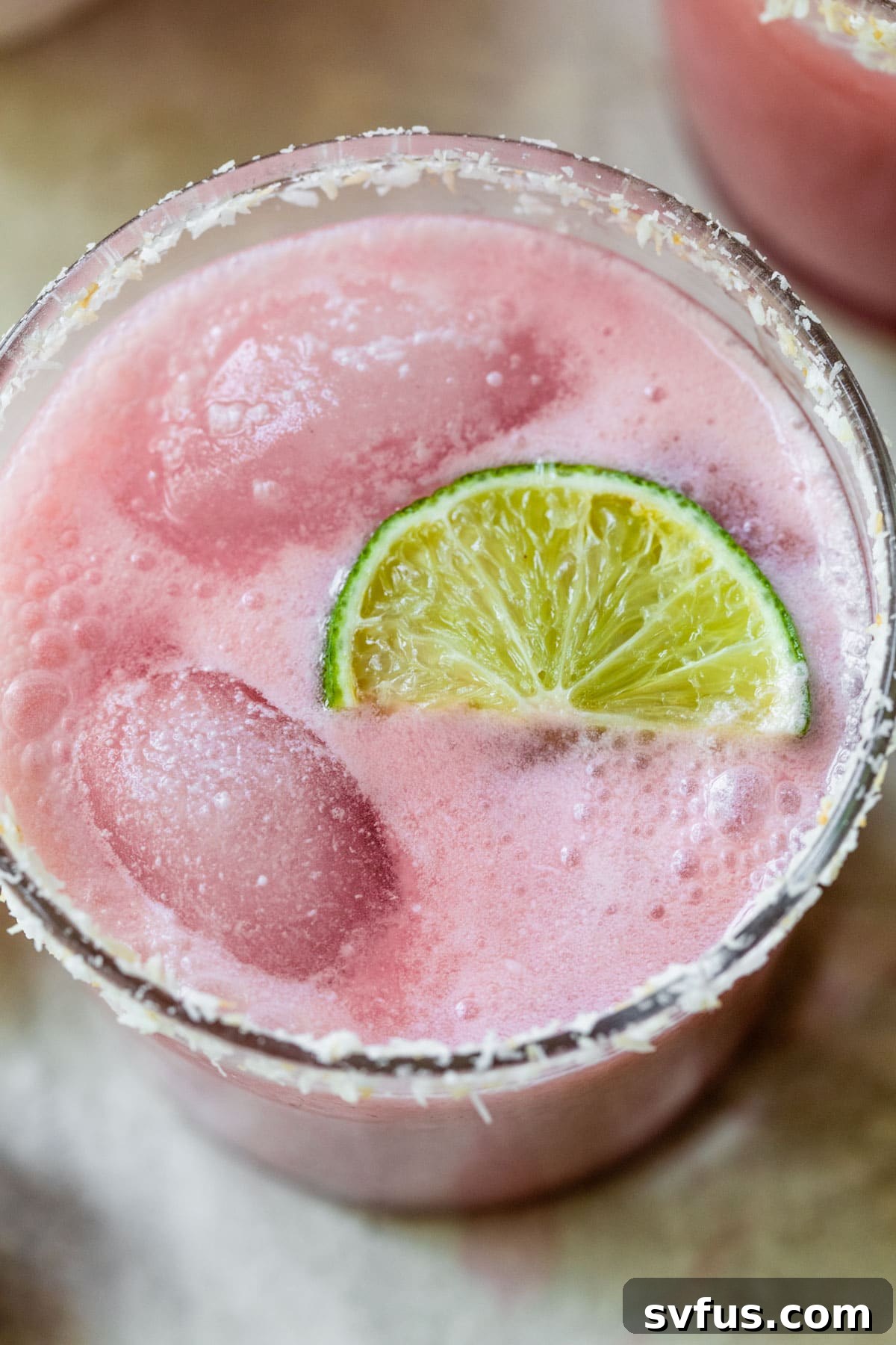 Close up photo of a pink-colored cocktail with a lime wedge in it, garnished with toasted coconut on the rim