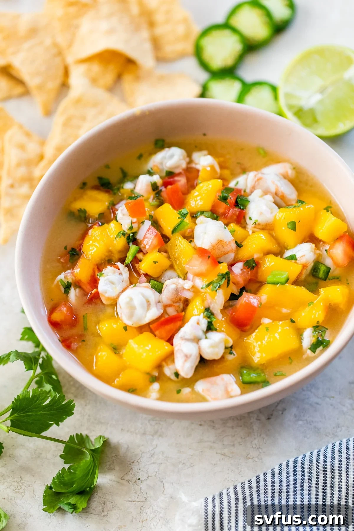 A beautifully arranged pink bowl of mango shrimp ceviche, accompanied by a pile of golden tortilla chips, suggesting a perfect pairing for this refreshing appetizer.