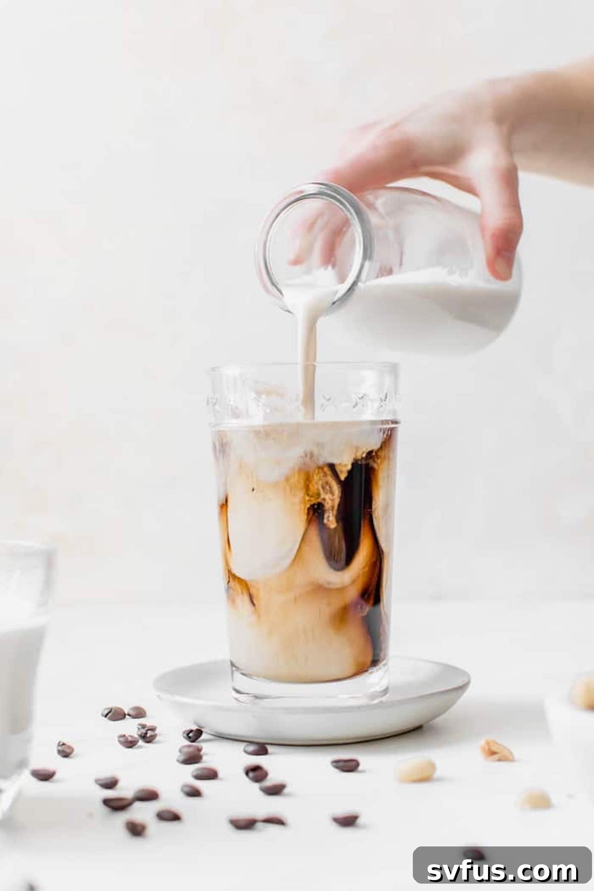 A hand pouring creamy homemade peanut milk from a jar into a glass.
