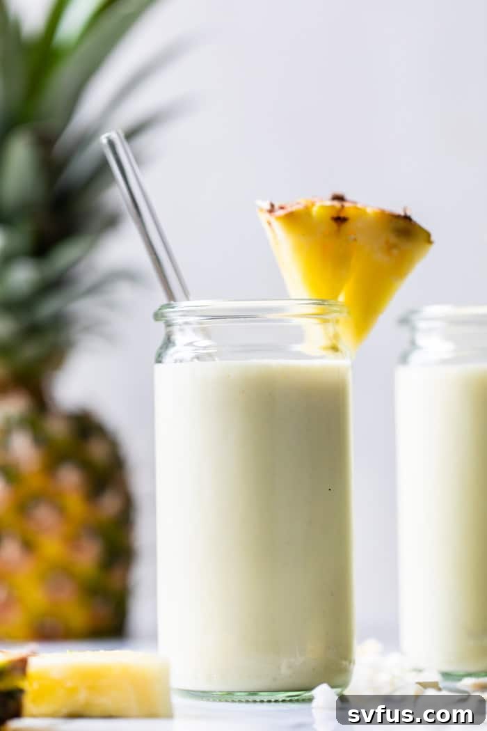A vibrant, creamy Piña Colada Smoothie in a tall glass, garnished with a fresh pineapple wedge, inviting you to a healthy tropical escape.